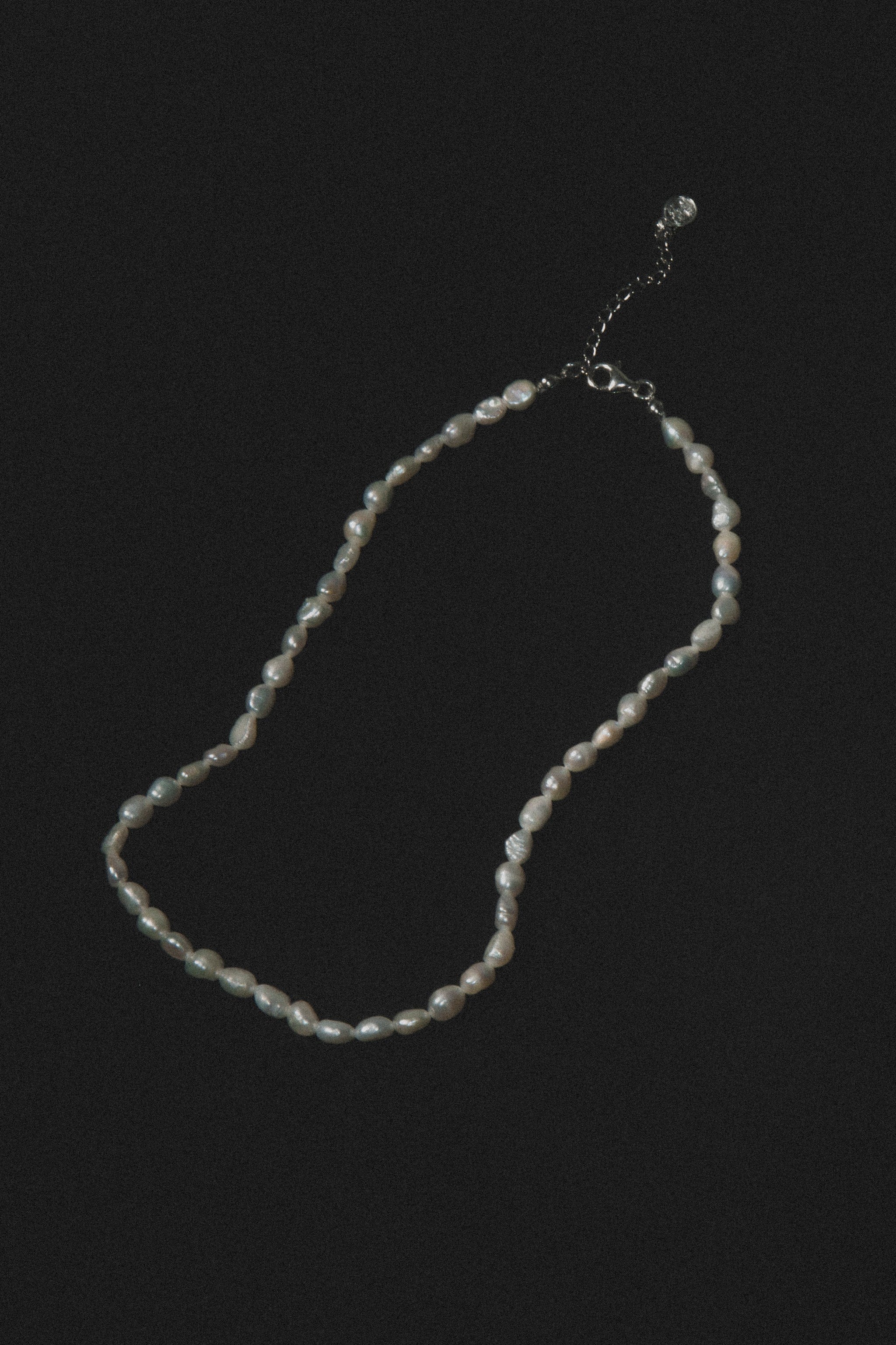 Strand of cream and gray pearl beads with silver-tone chain clasp and extension on black background.
