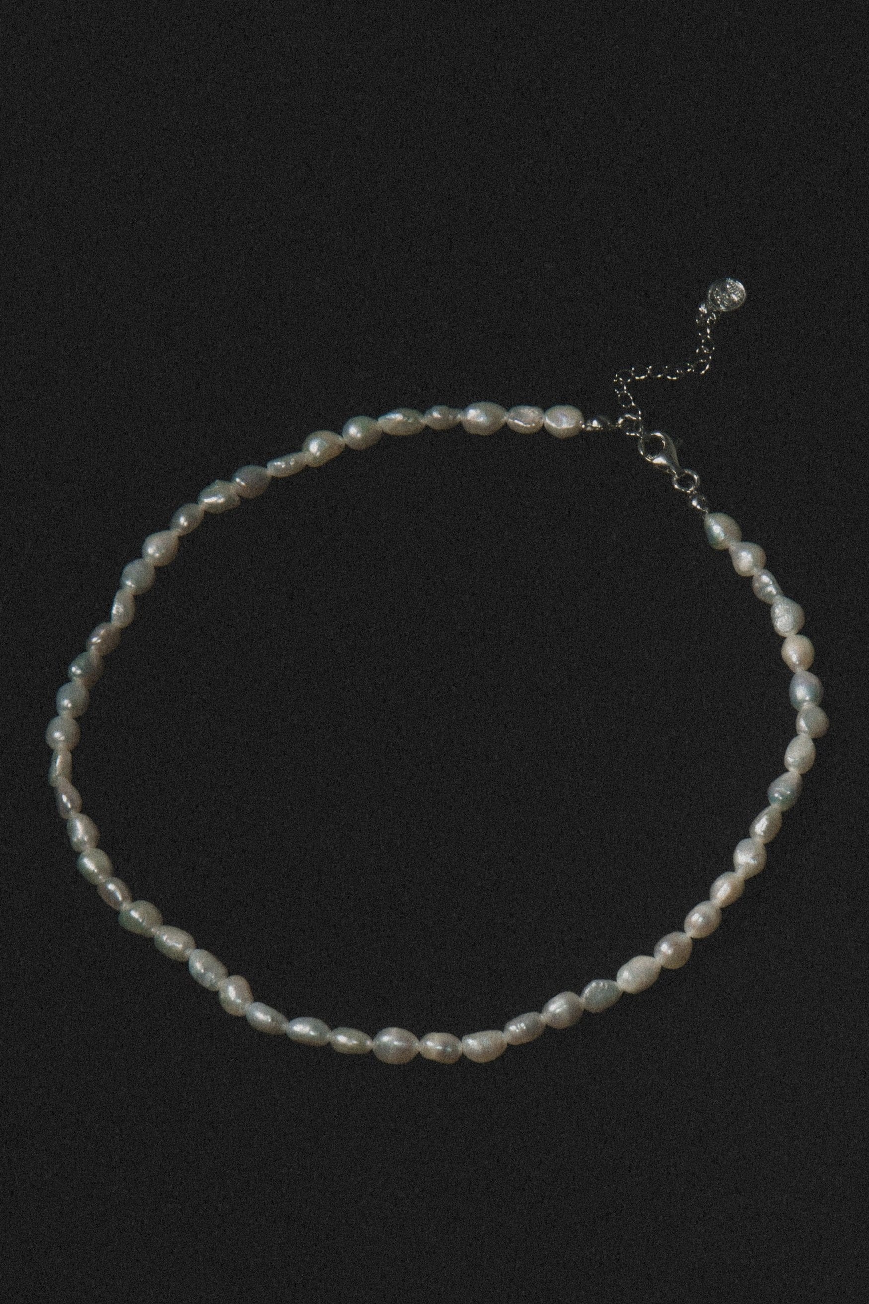 Strand of lustrous white pearls with silver-toned metal clasp and adjustable chain extension on black background.