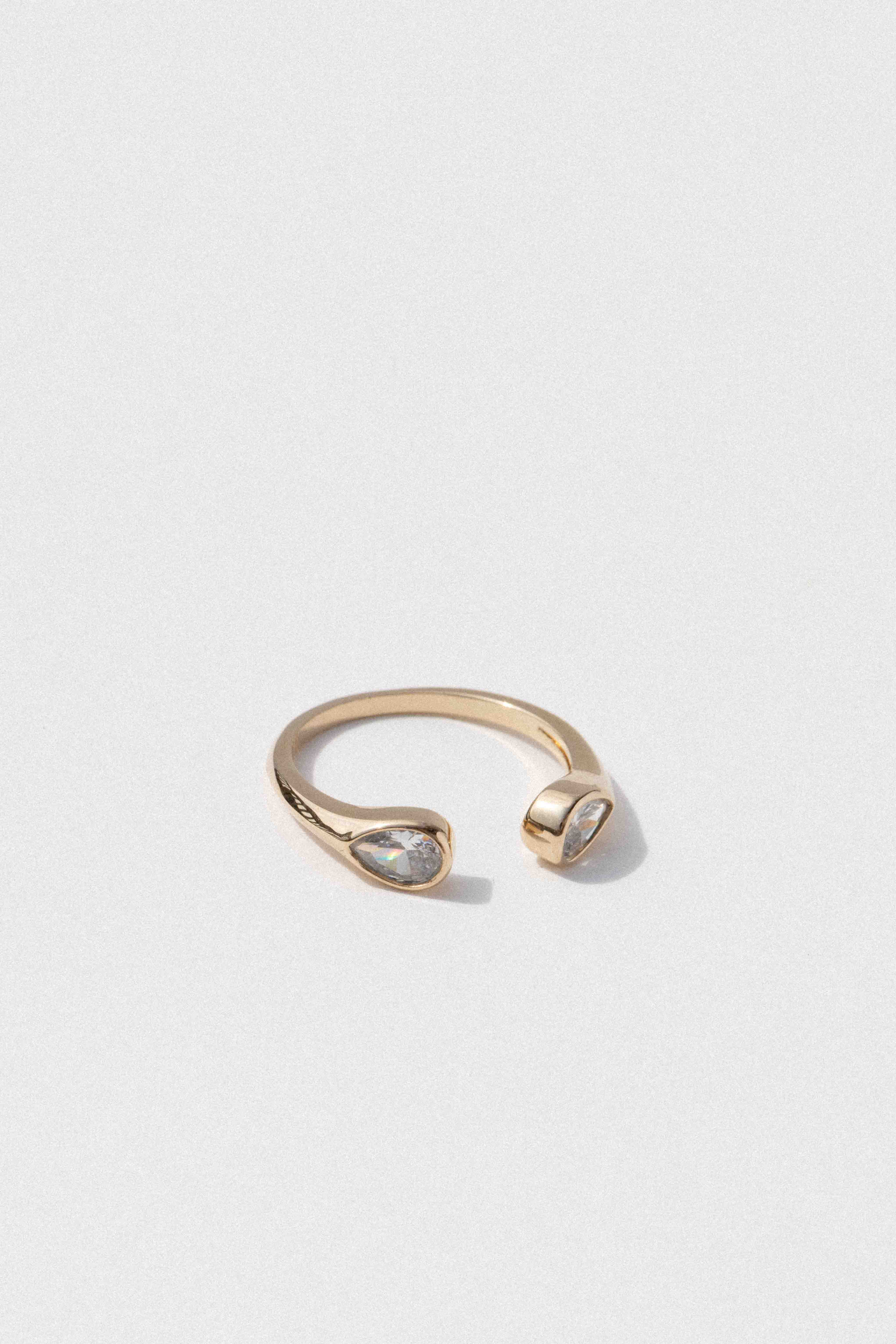 Gold-tone open ring with a teardrop-shaped clear crystal stone on one end and a polished rounded band on the other.