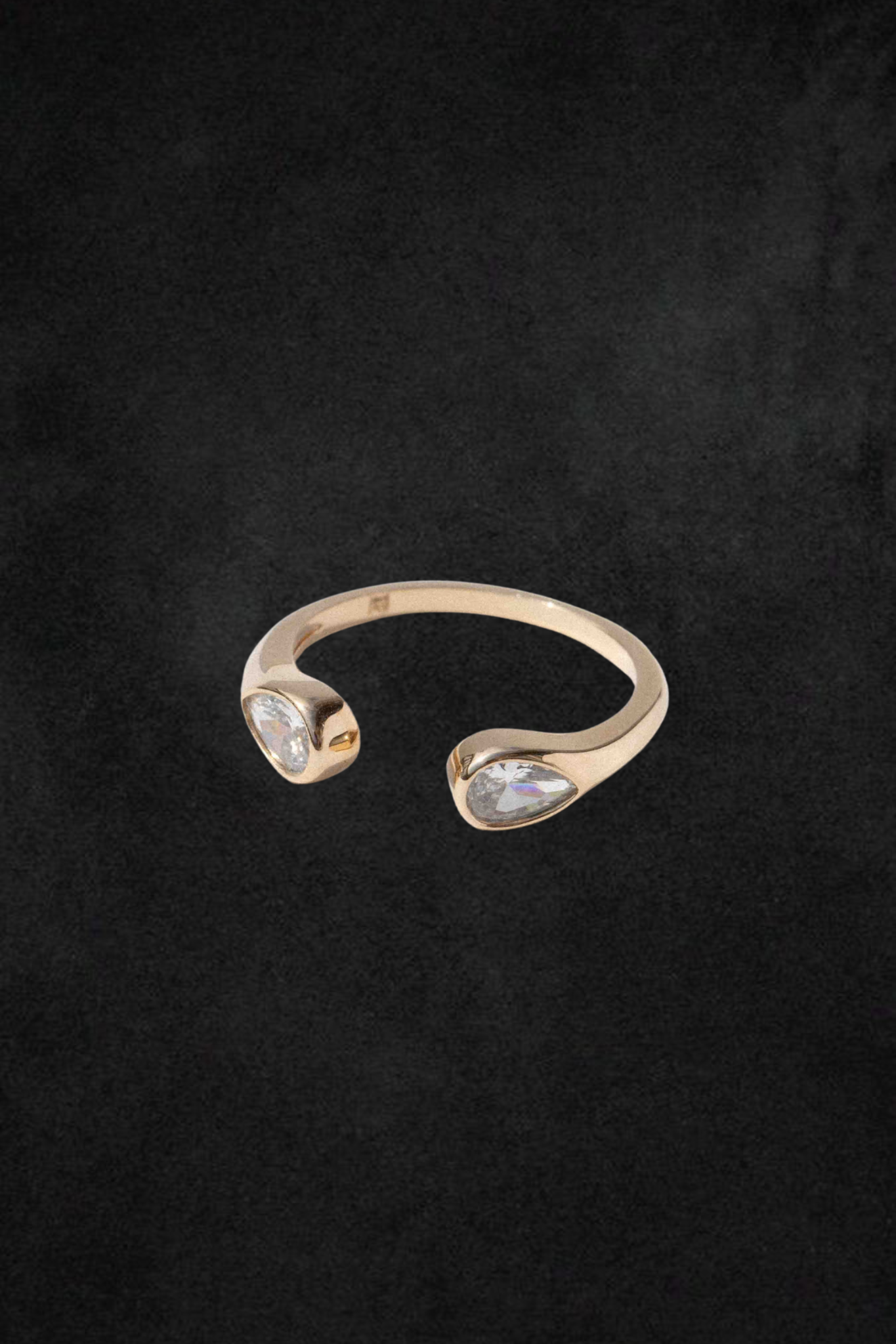 Gold-toned open ring with two teardrop-shaped cubic zirconia stones set at opposite ends against a dark background.