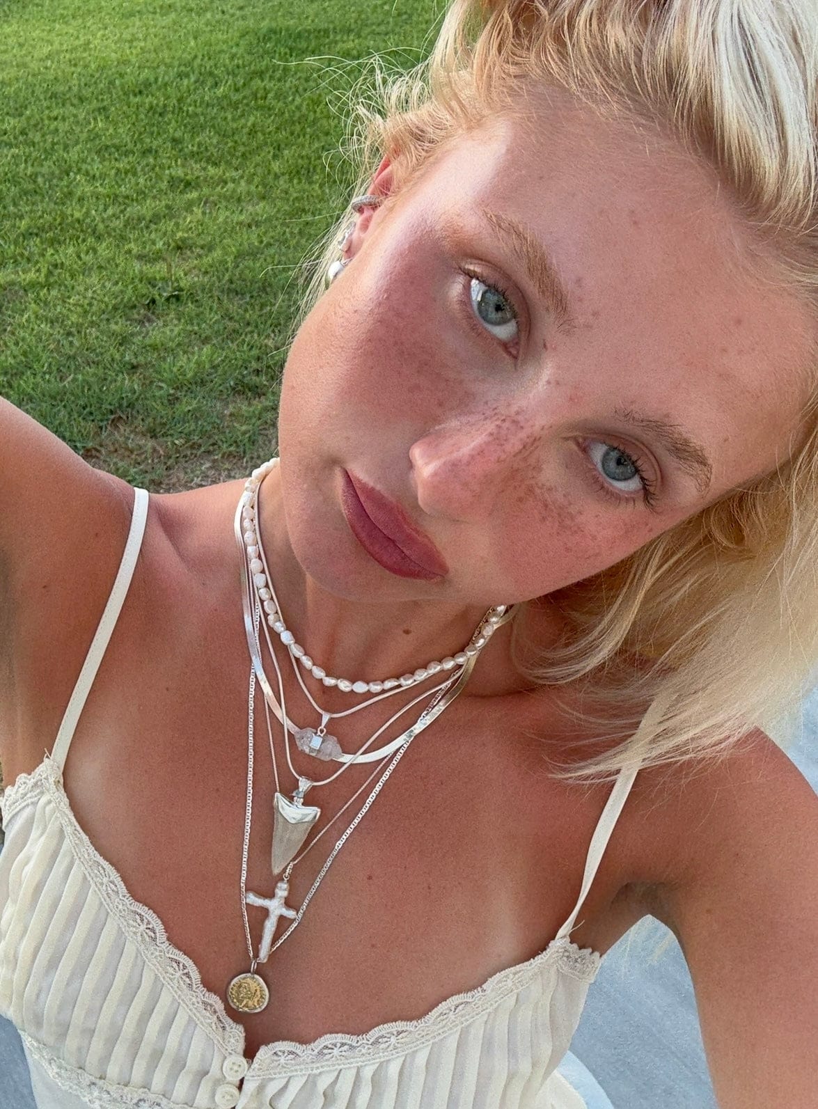 Woman wearing layered necklaces with pearl strands and silver chains with rectangular pendants.
