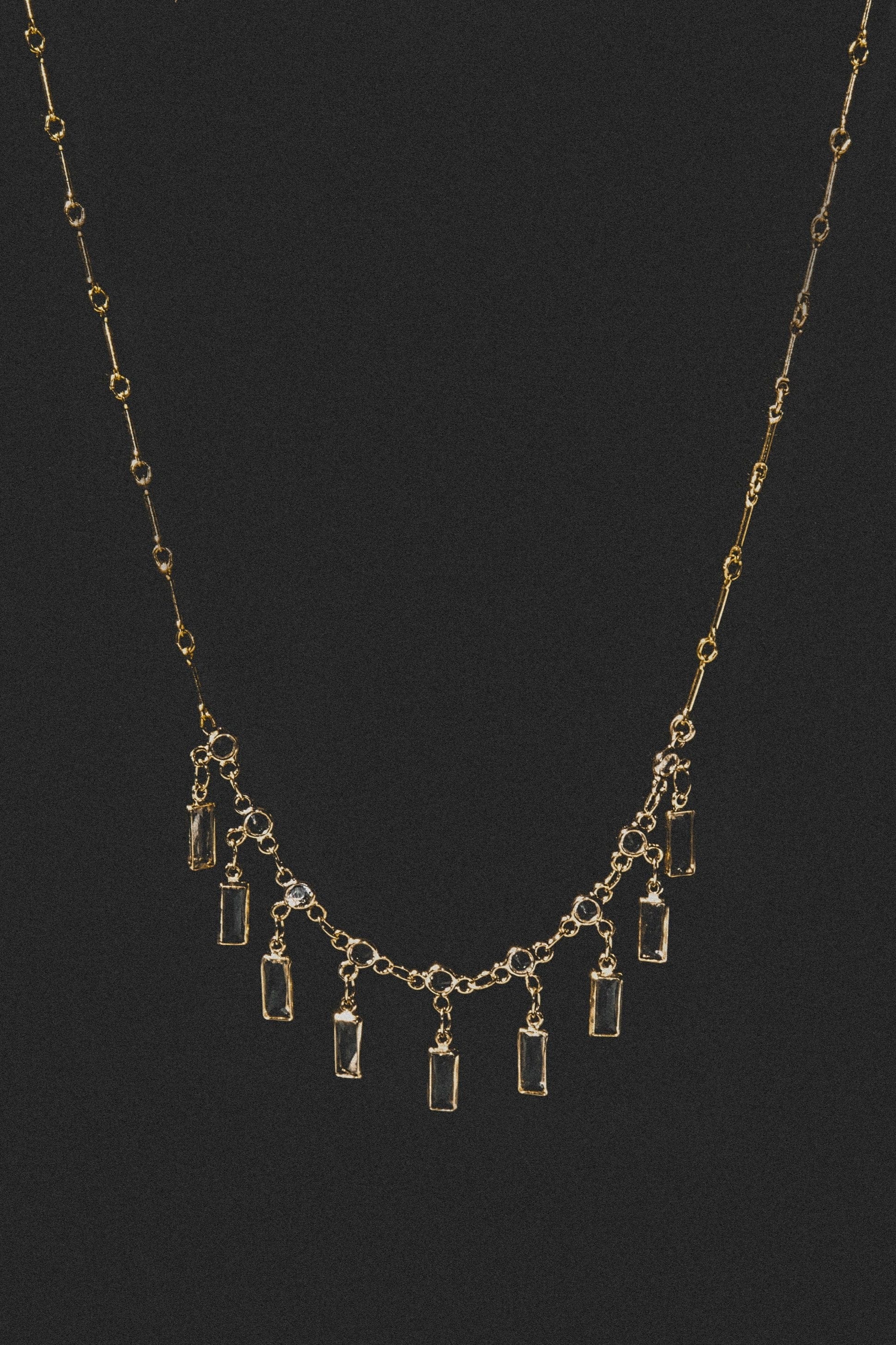Gold-tone necklace with station chain and rectangular crystal pendants arranged in descending arc pattern.