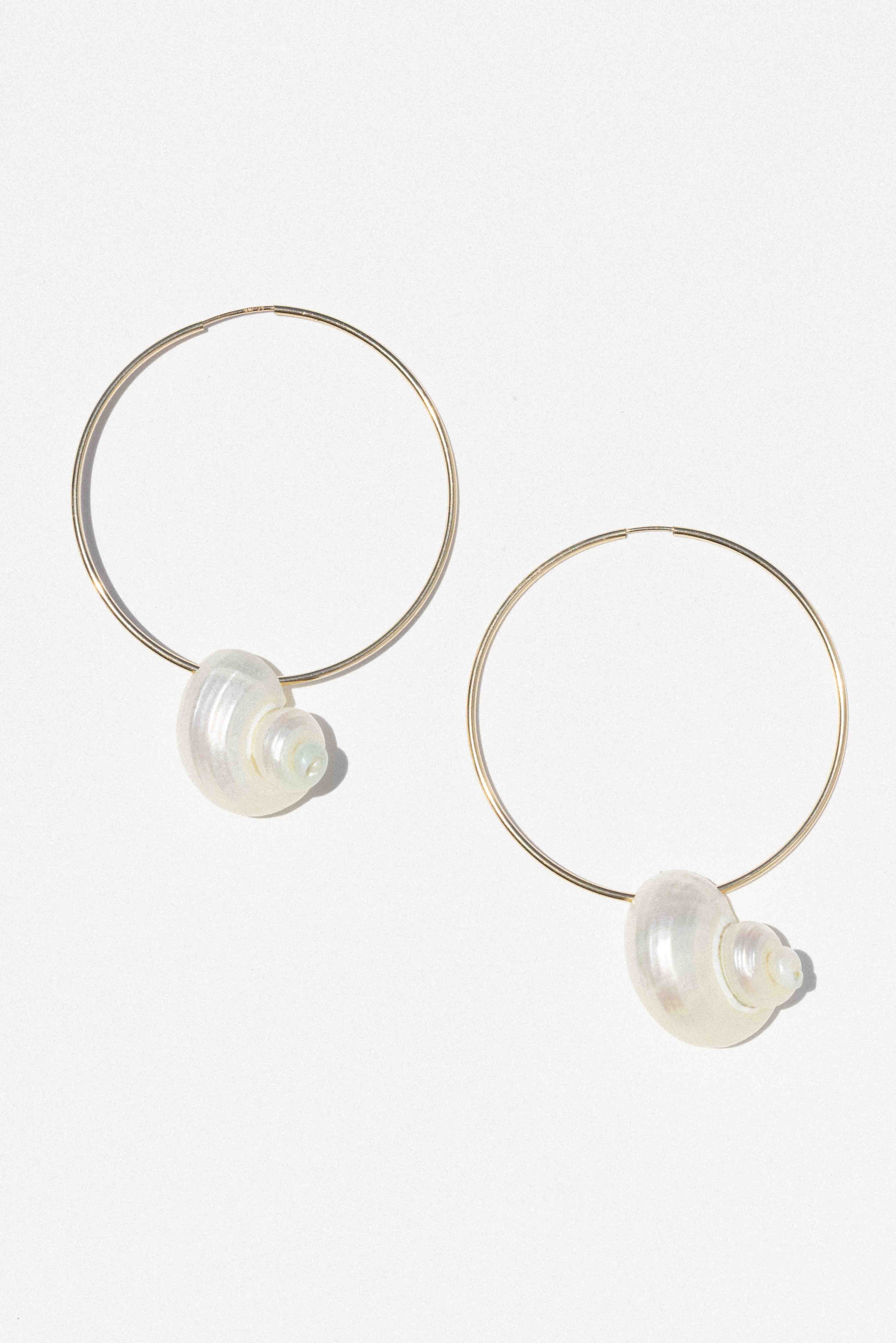Pair of thin metal hoop earrings with pearlescent spiral shell charms attached at the bottom.