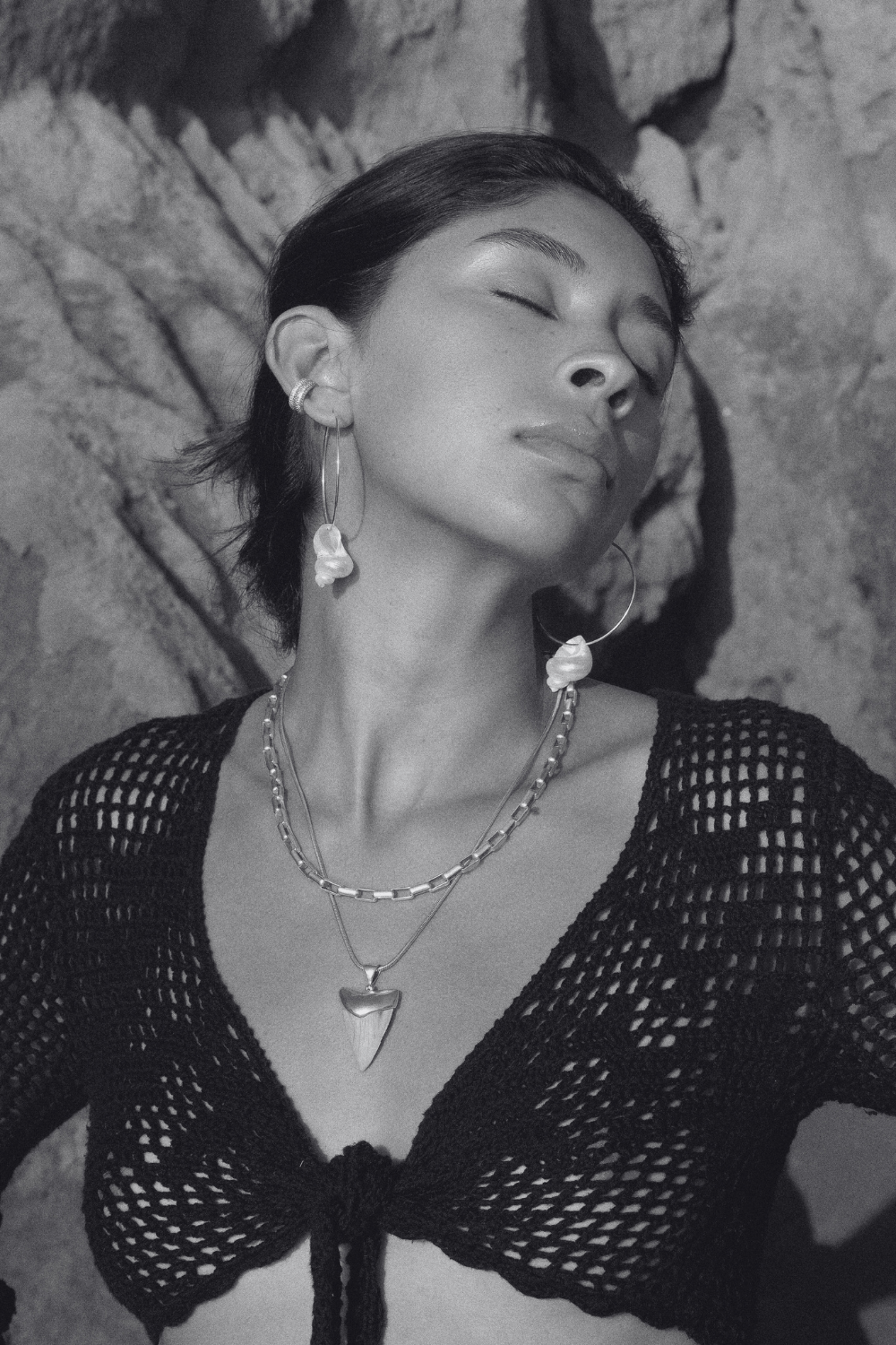 Silver-toned hoop earrings with shell pendants worn by woman against textured background.