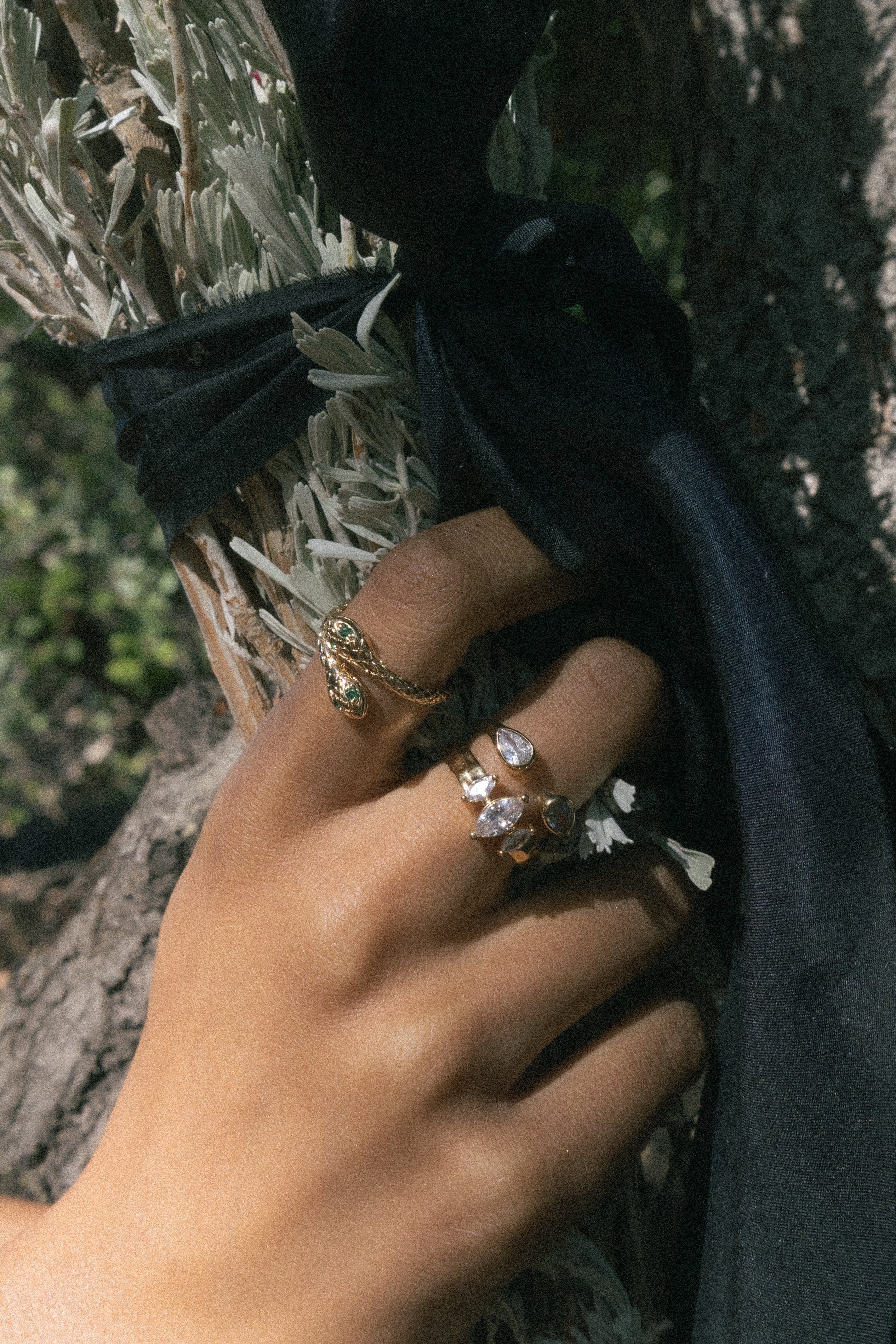 Gold-tone ring with oval cubic zirconia stone worn on hand against textured wall background.