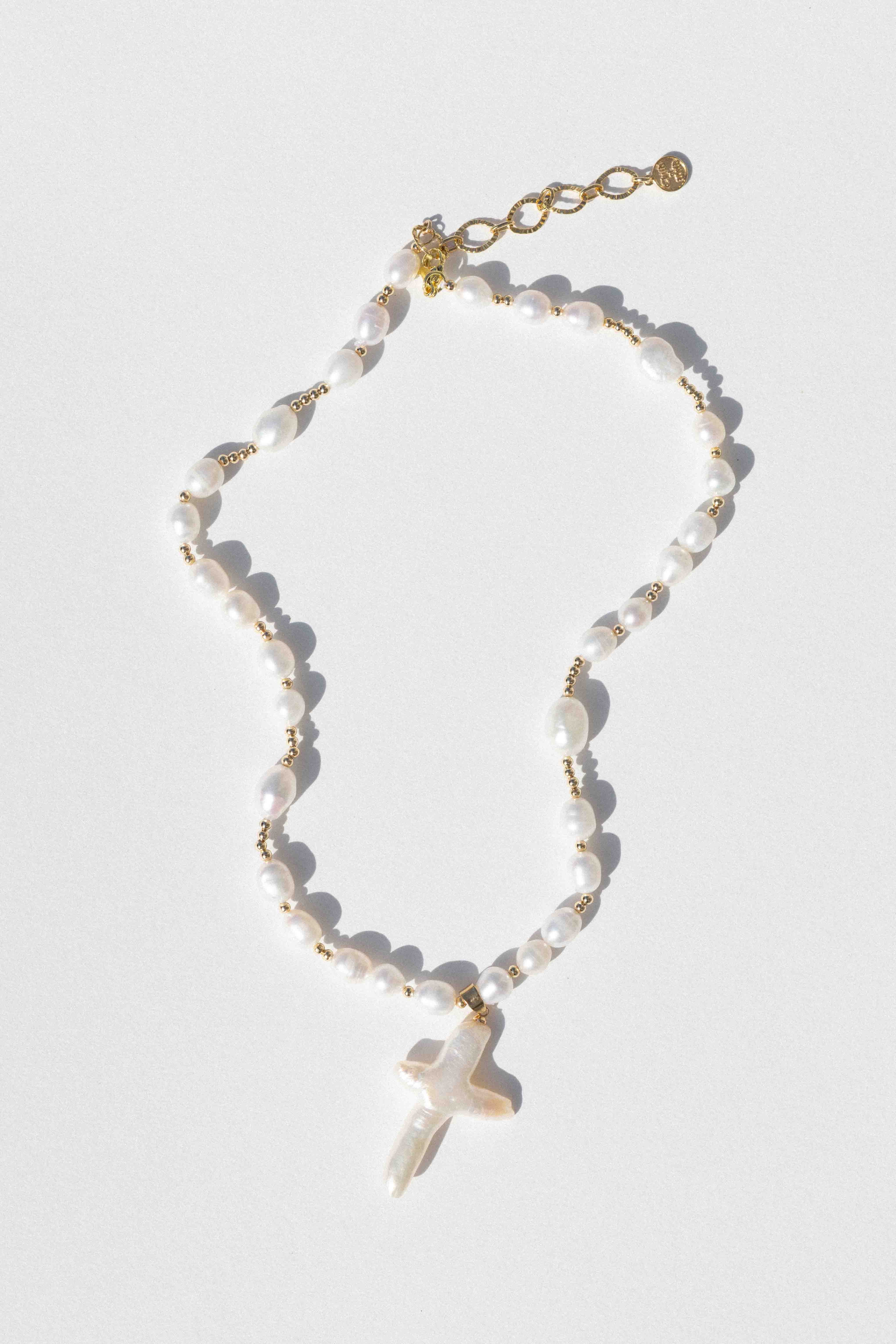 White pearl beaded necklace with gold-tone cross pendant and adjustable chain clasp.