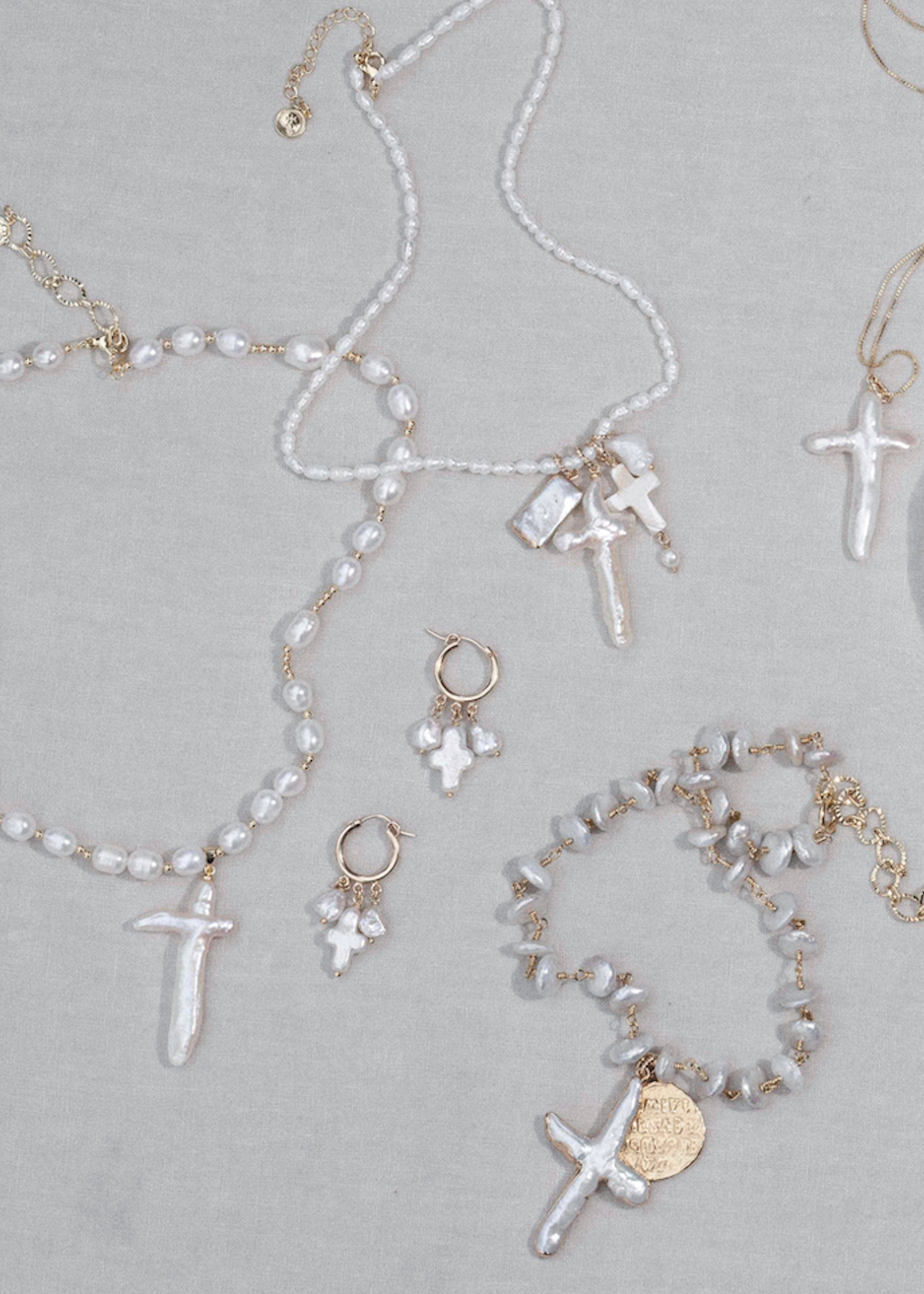 Gold-tone and white pearl necklaces with cross pendants and matching earrings displayed on gray surface.