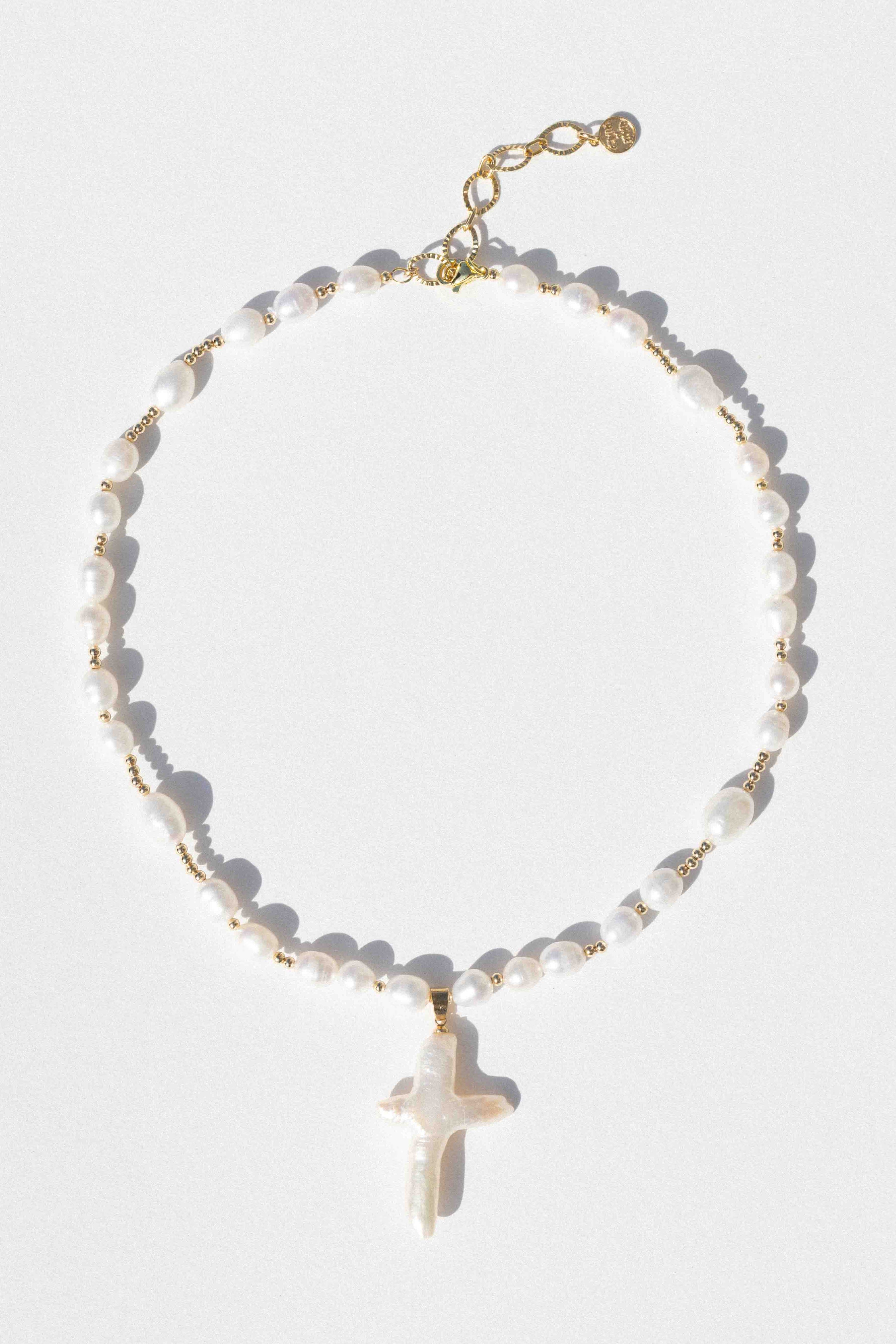 White pearl beaded necklace with gold spacers and a white pearl cross pendant with gold chain closure.