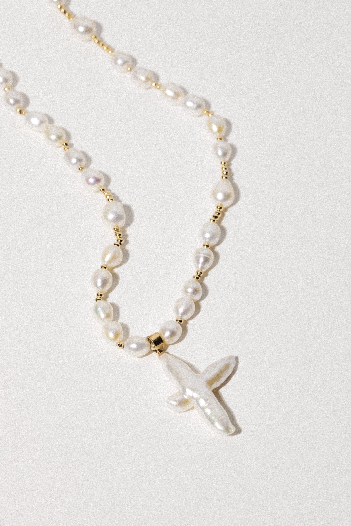 Gold-tone necklace with cream pearls separated by gold spacers and a cross-shaped pearl pendant.