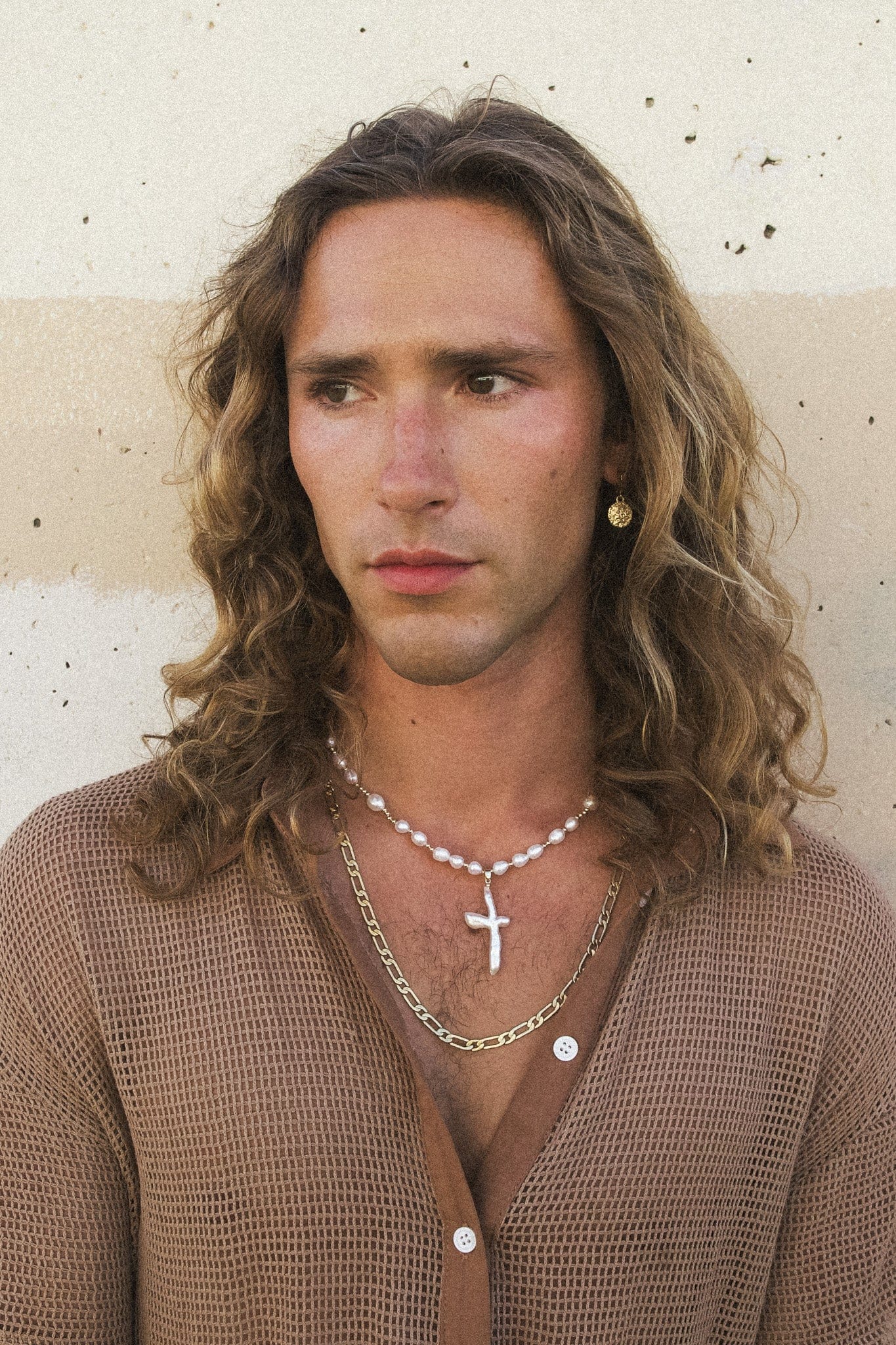 White pearl beaded necklace with cross pendant worn layered with a chain necklace.