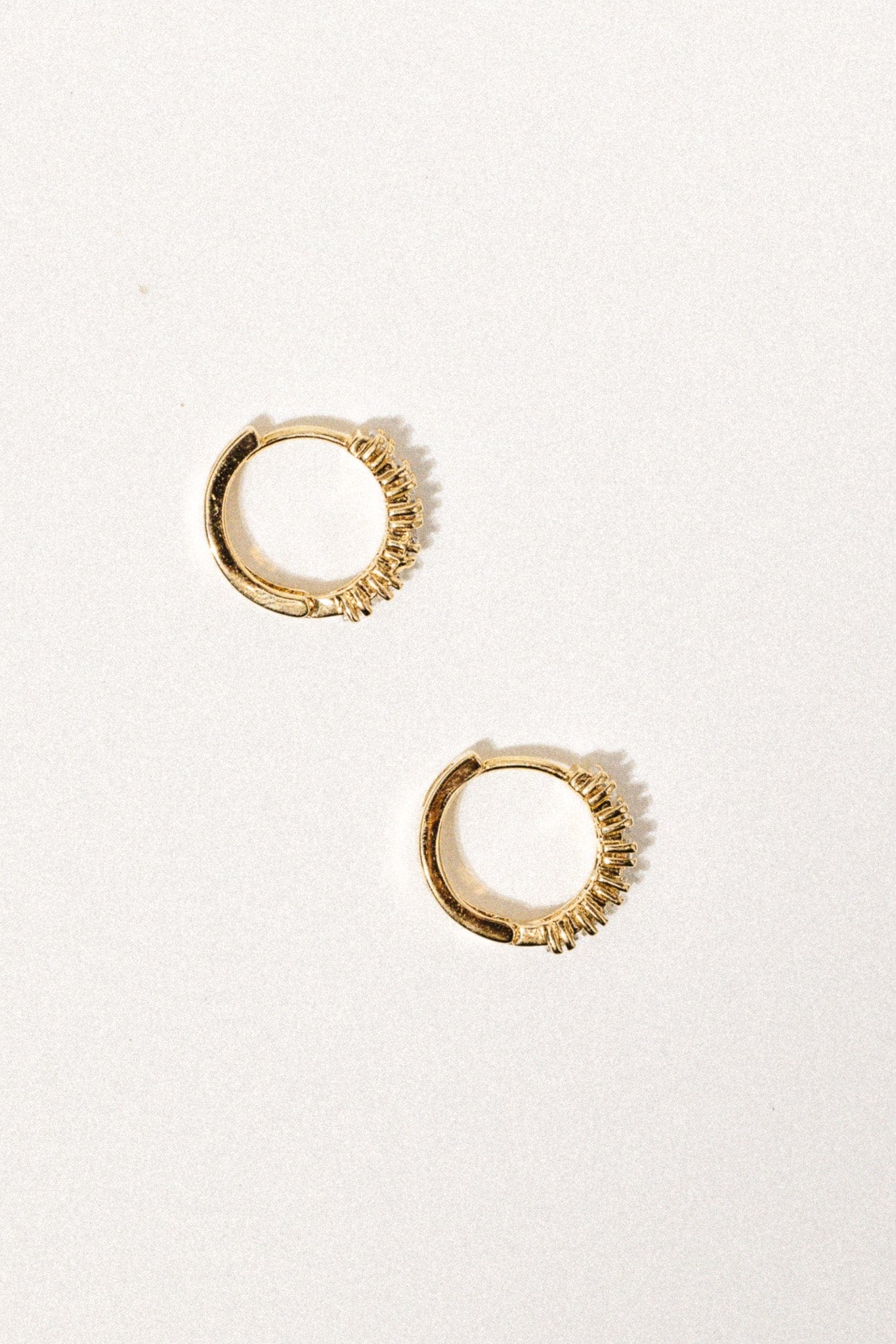 Pair of gold-toned huggie earrings with textured ribbed detailing on half the hoop.