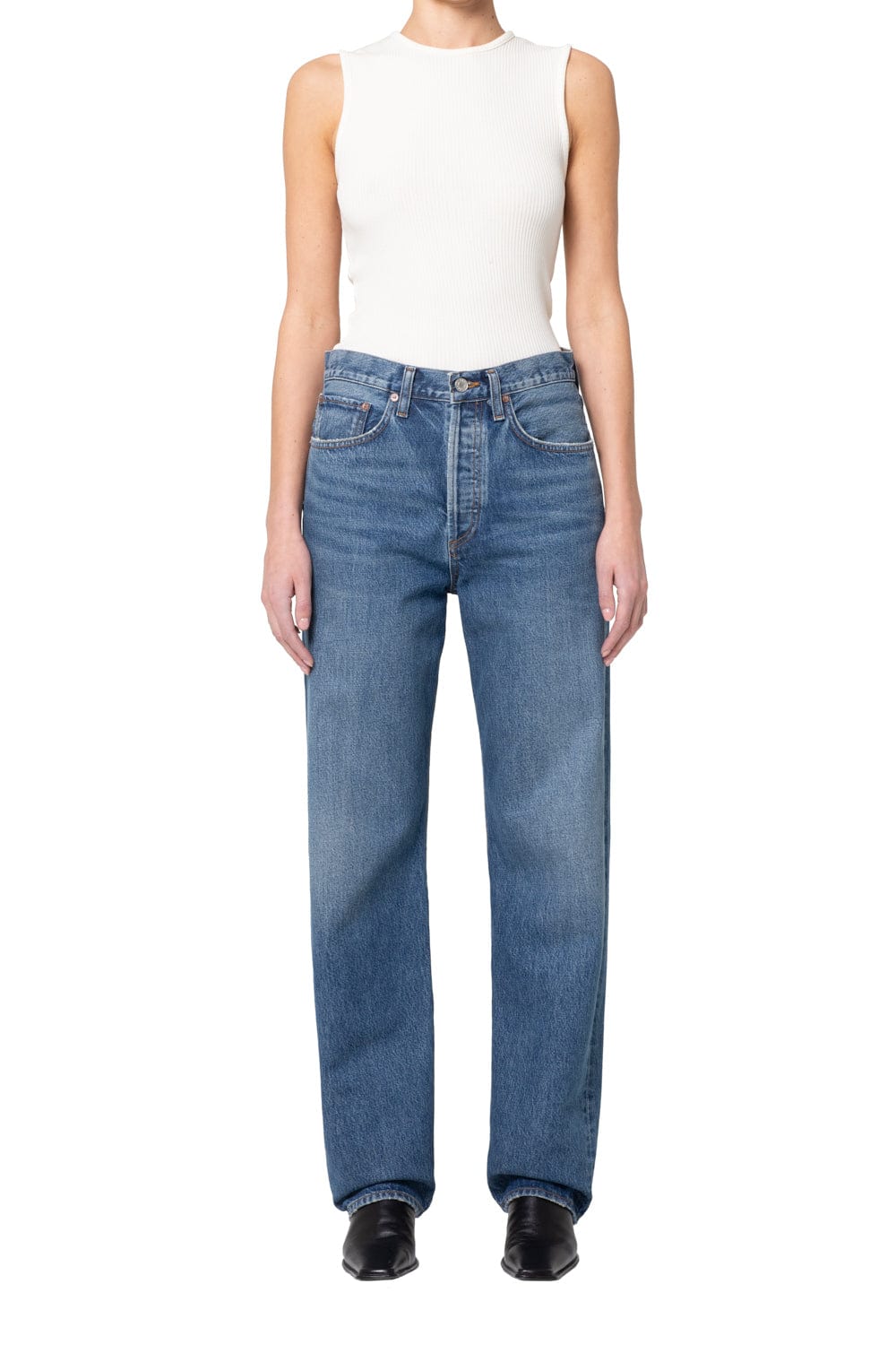 Woman wearing white sleeveless ribbed tank top and blue medium-wash straight-leg jeans with black shoes.