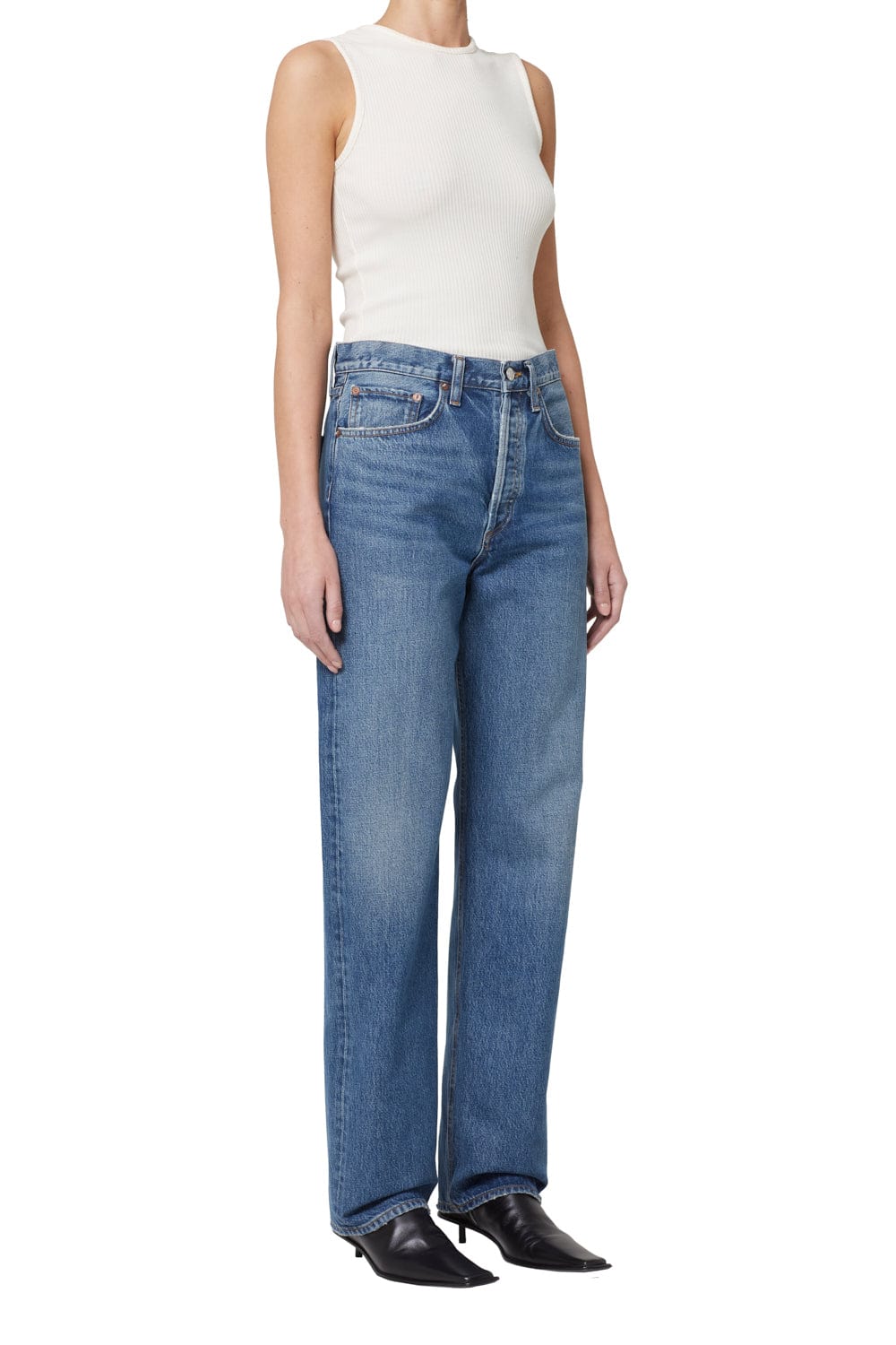 Woman wearing a white sleeveless ribbed tank top and medium-wash straight-leg denim jeans with black pointed-toe shoes.