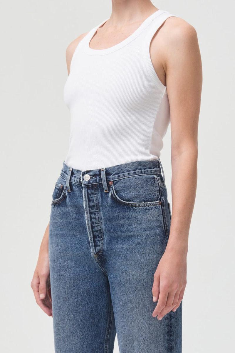White ribbed sleeveless tank top with crew neckline worn with blue denim jeans.