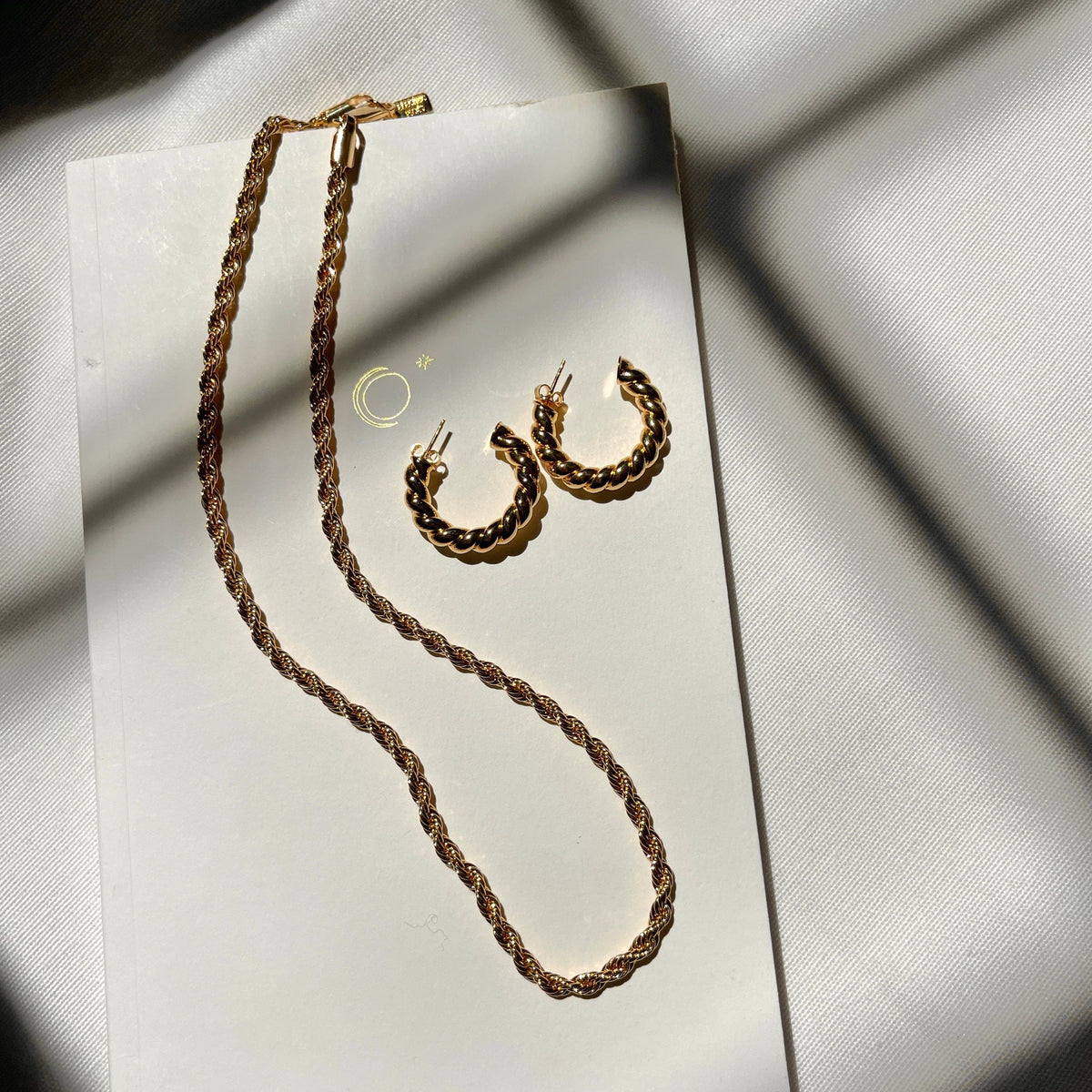 Gold-tone twisted rope necklace with matching twisted hoop earrings displayed on white card.