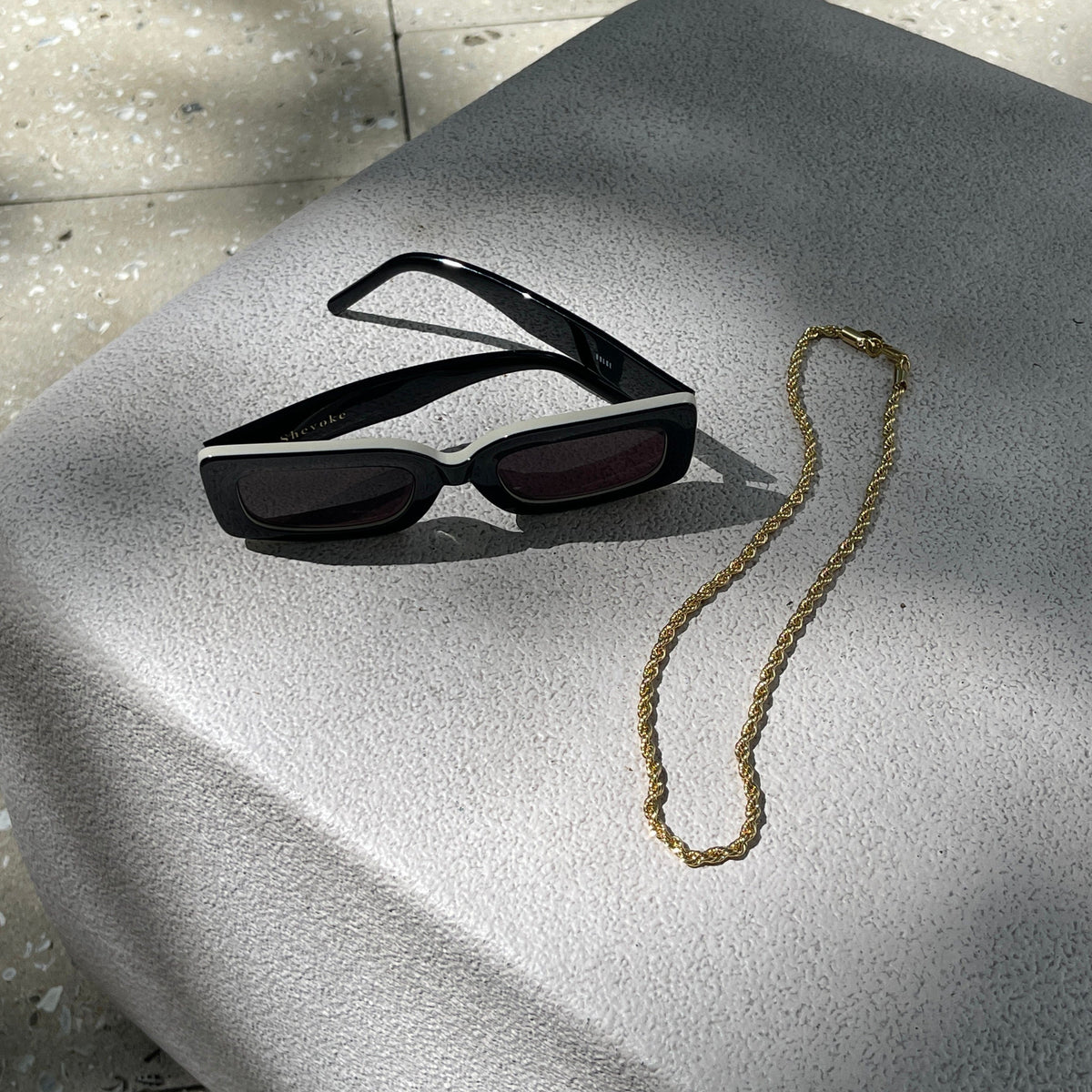 Gold-toned twisted chain necklace, 18 inches long with 4mm links, displayed next to black sunglasses.
