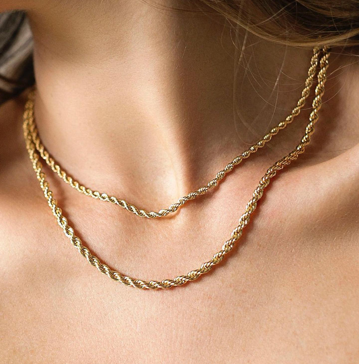 Gold twisted rope chain necklace worn layered on a person's chest.