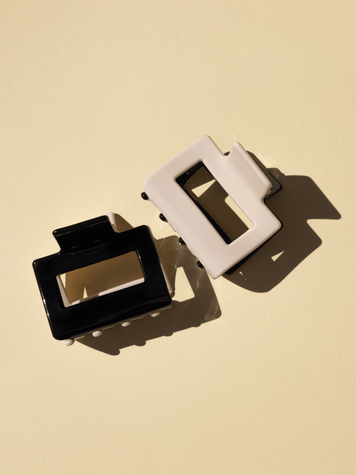 Two rectangular hair clips in nude and black with metal accents, displayed on a neutral background.