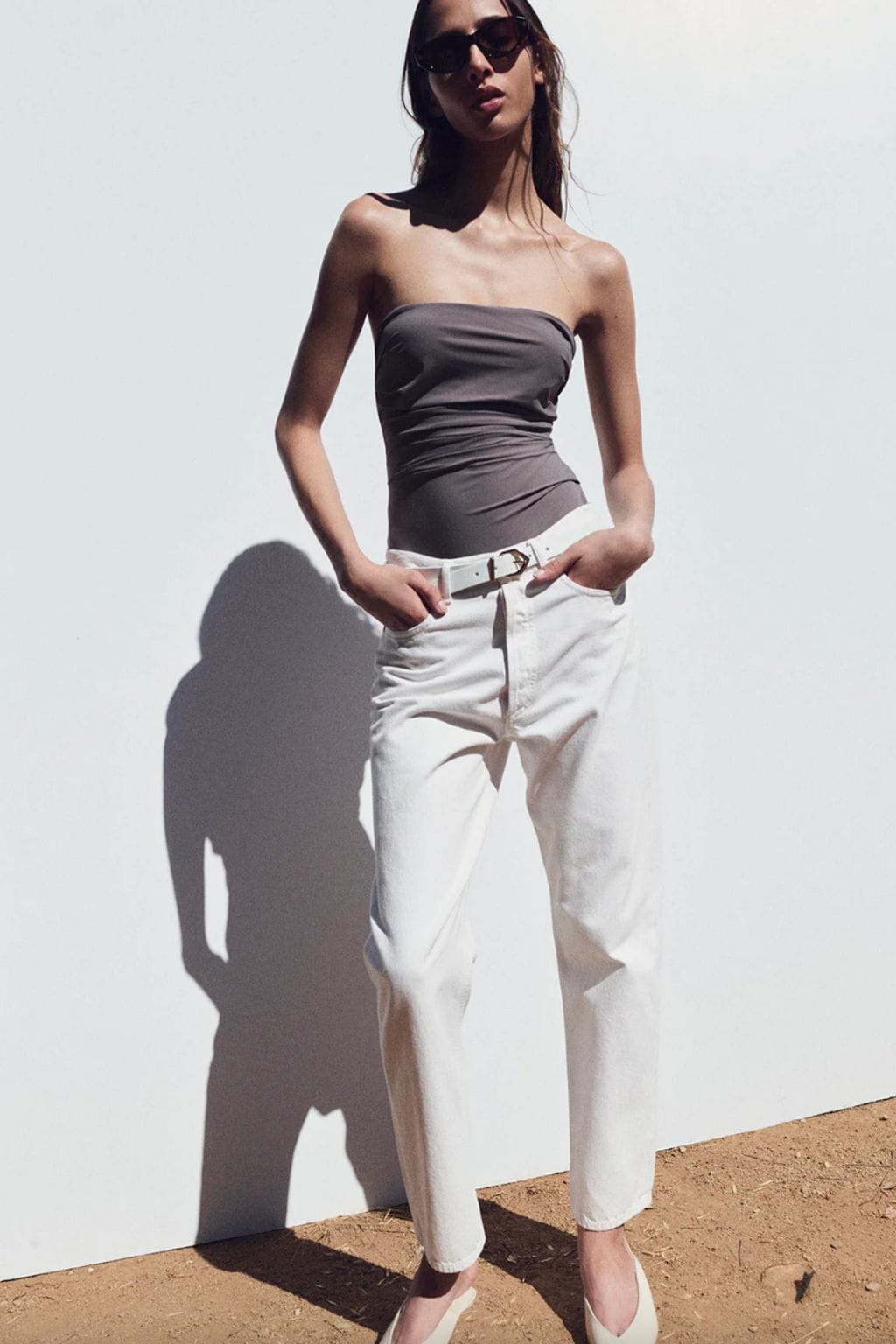 Woman wearing white high-waisted jeans with a white belt and black strapless top, styled with sunglasses.