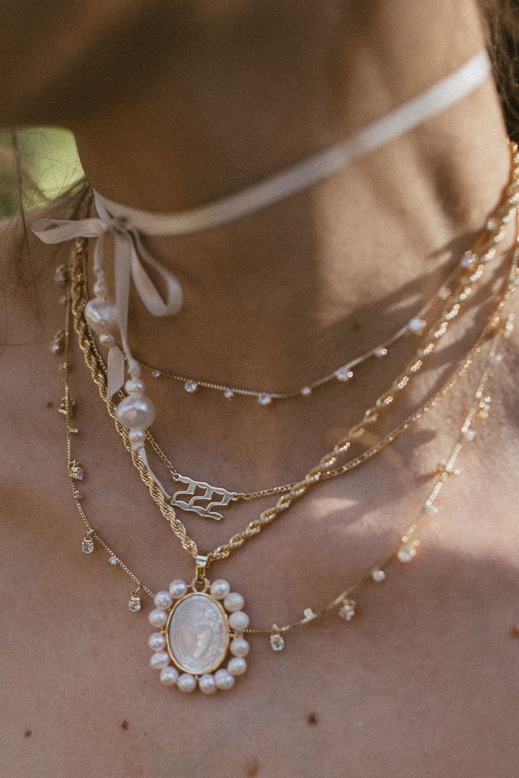 Gold necklace with oval pearl-framed pendant featuring angel number 222 design, worn layered on neck.
