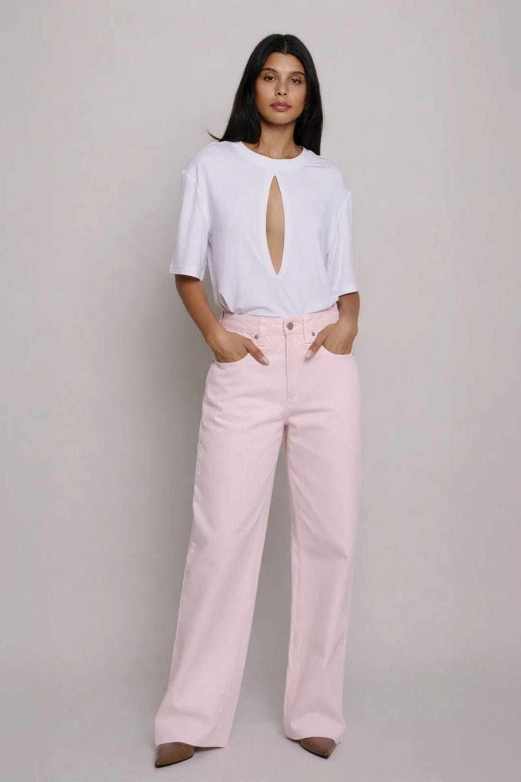 Woman wearing white short-sleeve top with front cutout and light pink wide-leg jeans.