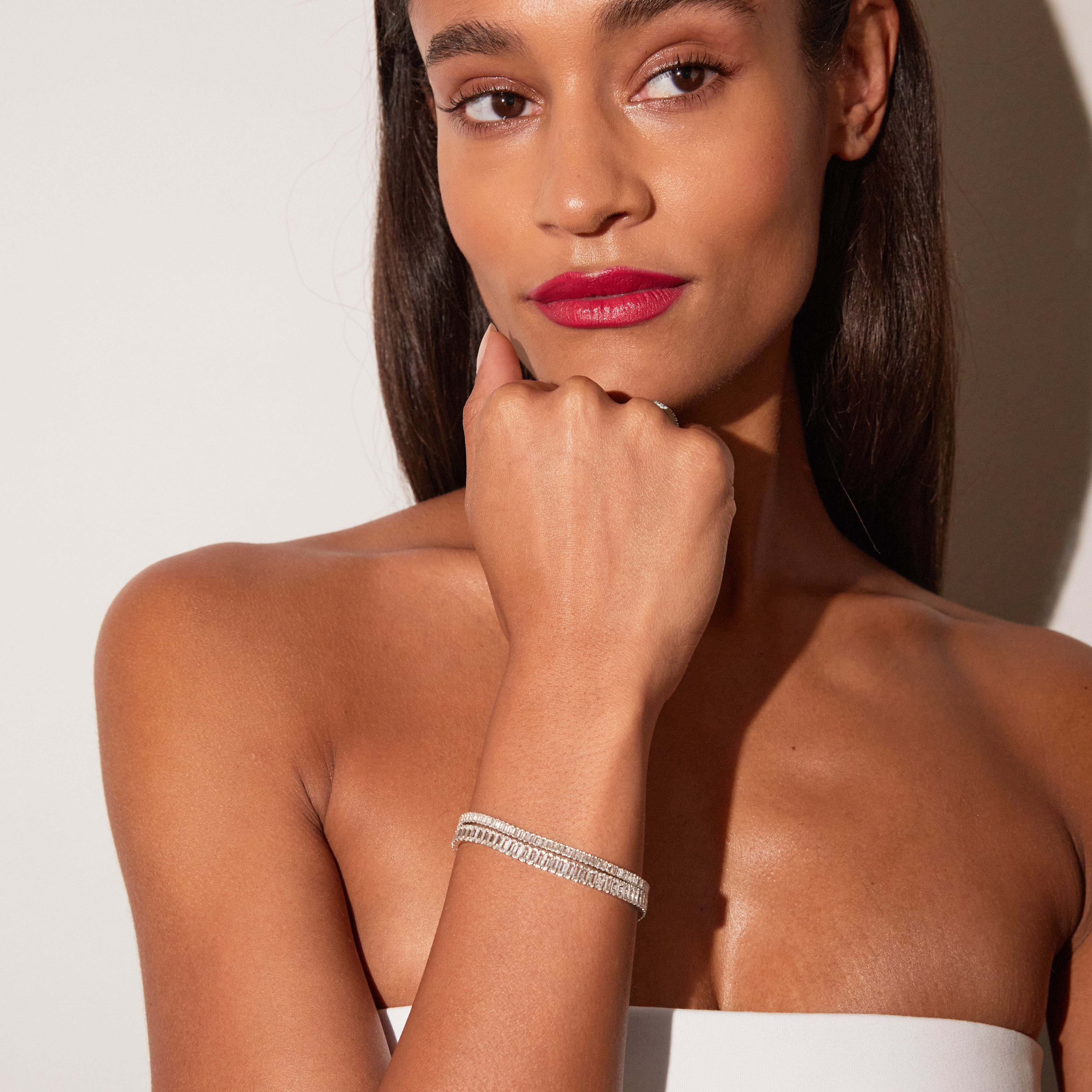 White sapphire baguette tennis bracelet worn on wrist with rectangular stones in metal setting.