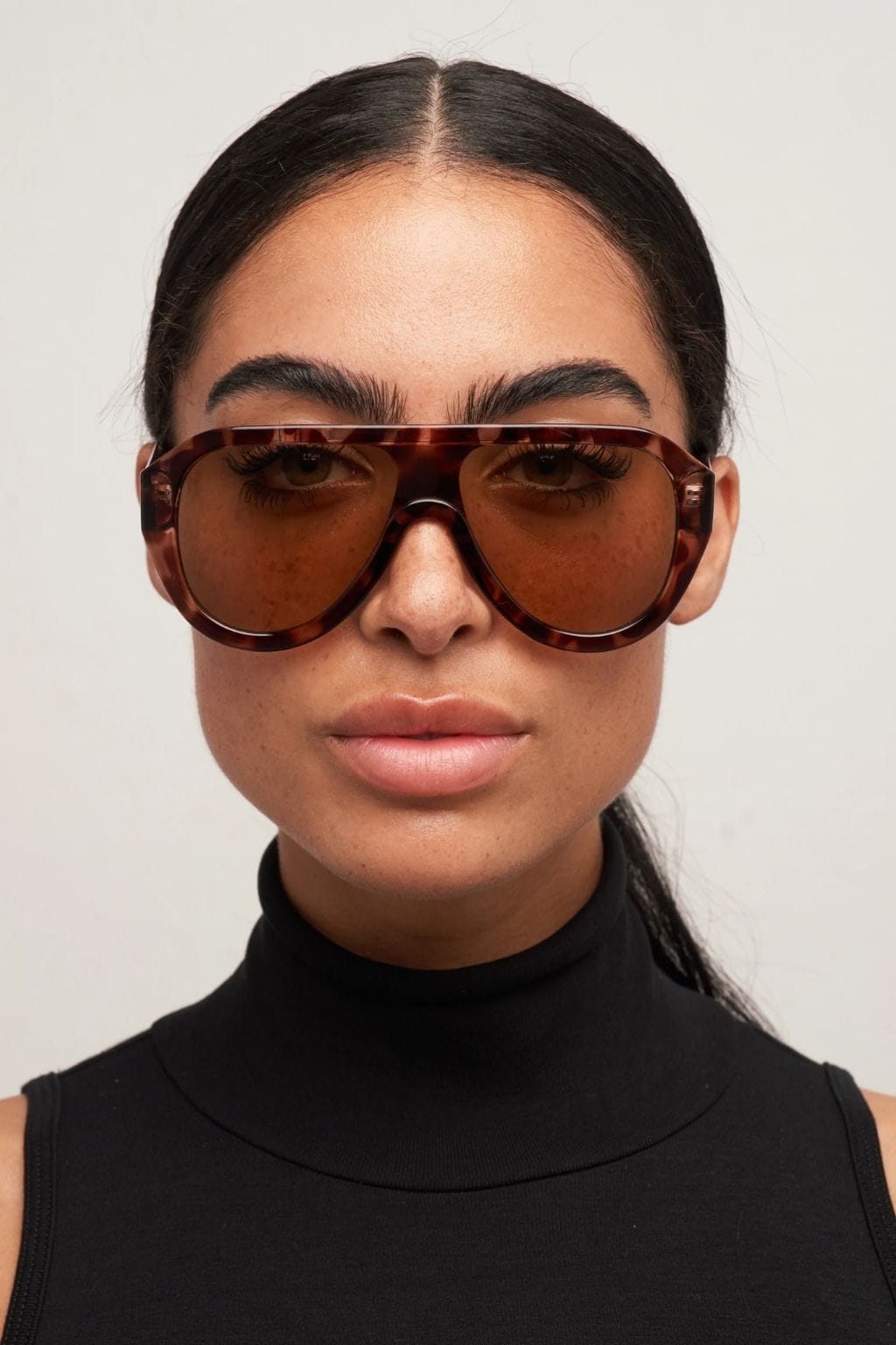 Brown tortoiseshell oversized aviator sunglasses with tinted lenses worn by a person in a black turtleneck.