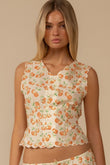Sleeveless cream vest with orange cherry print and scalloped edges on neckline and hem.