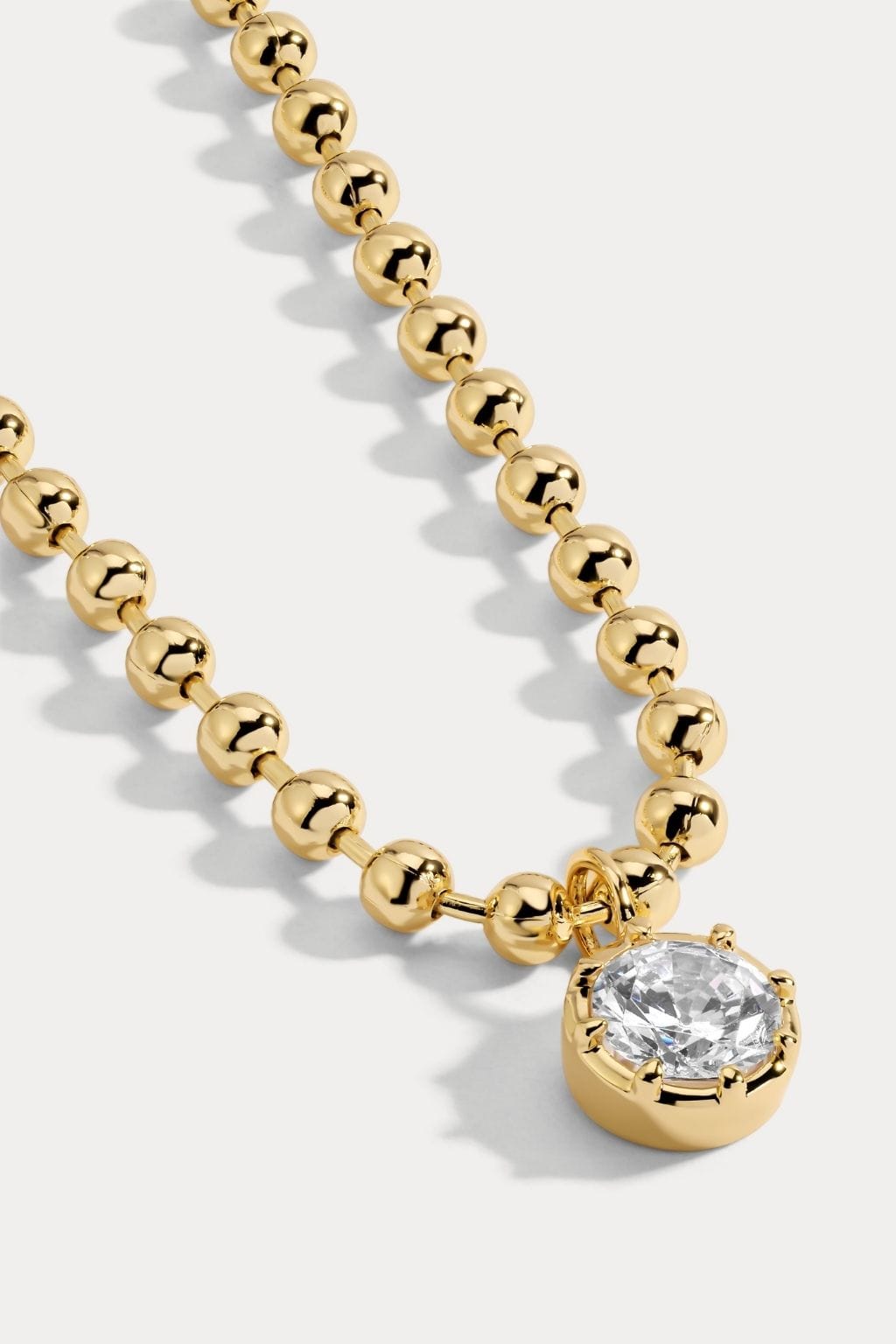 Gold ball chain necklace with round crystal pendant.