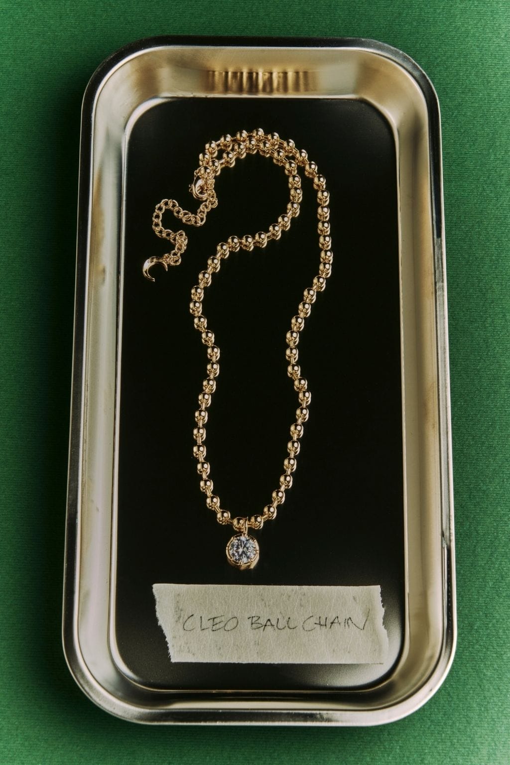 Gold-toned ball chain necklace with small round pendant displayed in branded packaging on black insert.