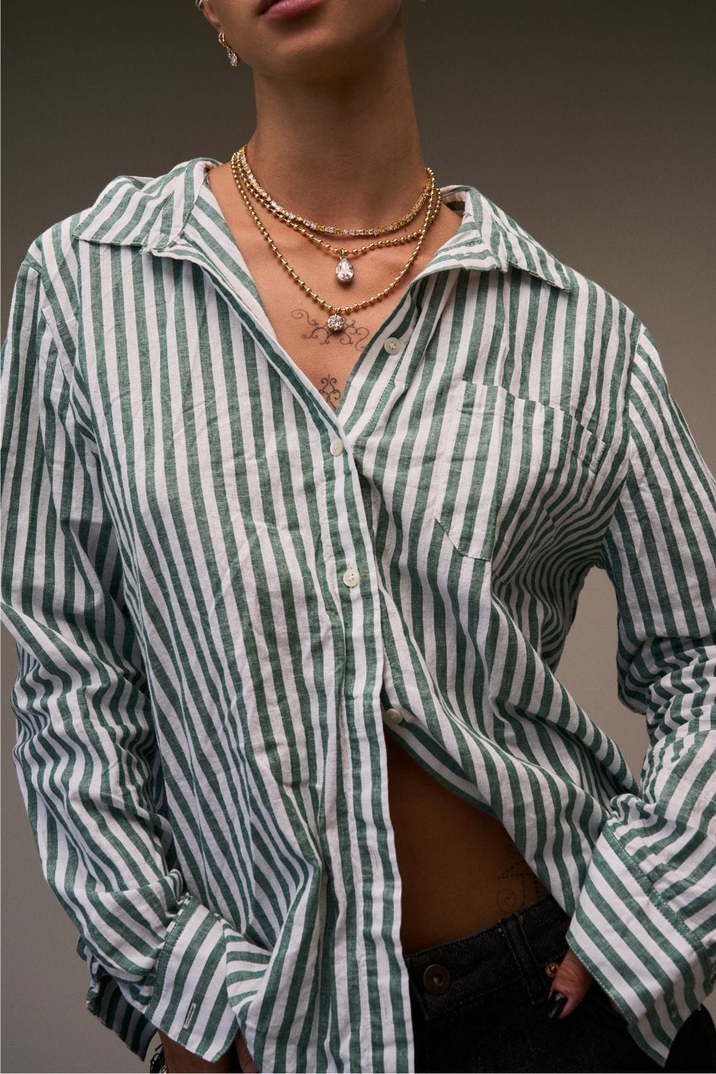 Gold ball chain necklace worn layered with a pearl pendant on a model in a striped shirt.