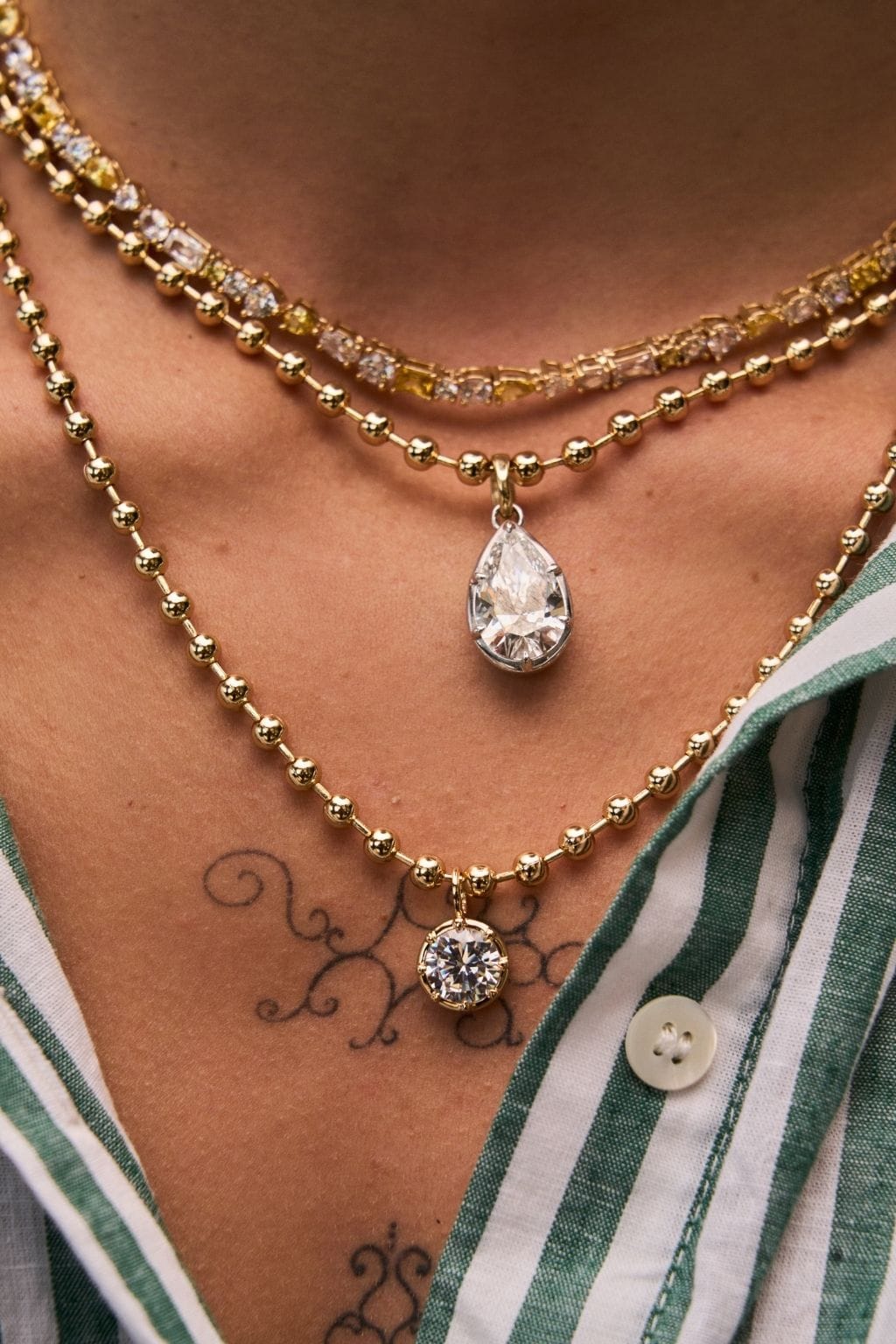 Gold ball chain necklace worn layered with crystal teardrop and round crystal pendants.