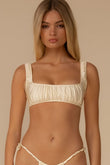 Cream bikini top with square neckline, gathered fabric, and thick shoulder straps on model against neutral background.