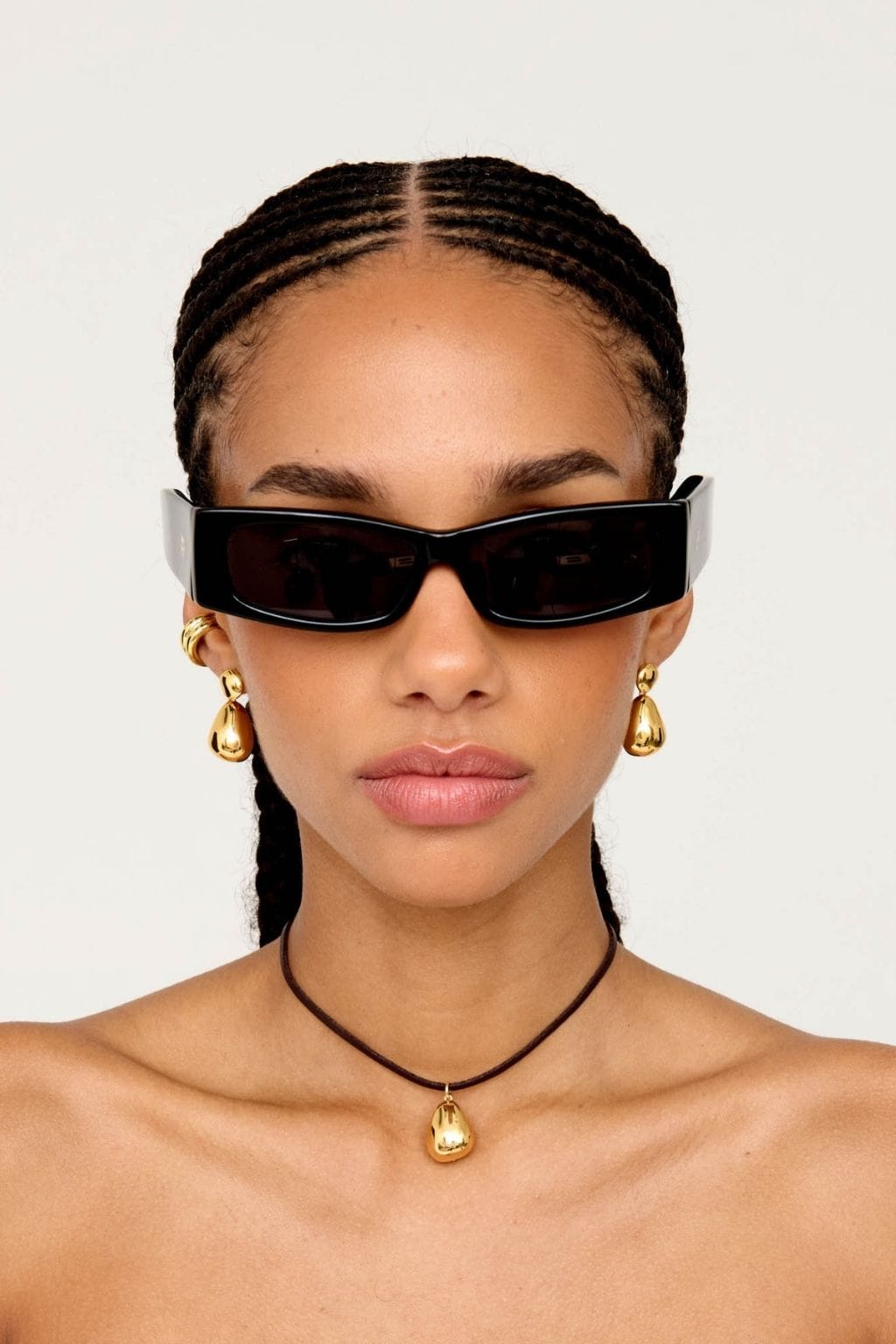 Gold-tone teardrop earrings worn on a model's ears, paired with a matching pendant necklace.