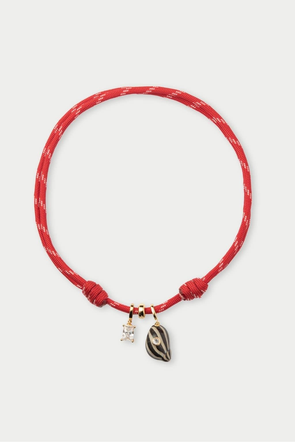 Red braided cord necklace with knotted ends and two pendant charms: a clear crystal and a striped oval stone.