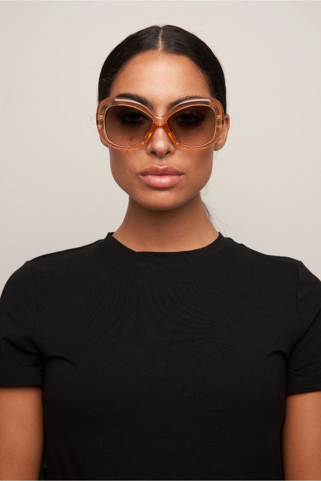 Clear plastic square sunglasses with gradient brown lenses worn by person in black t-shirt.