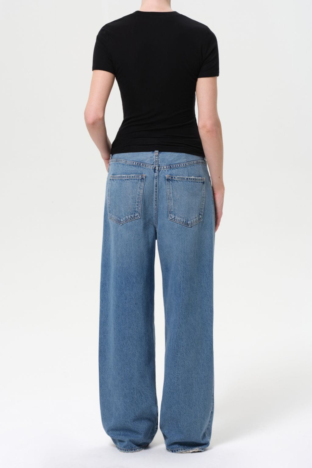 Woman wearing black short-sleeve top and light blue pleated baggy jeans, shown from behind.