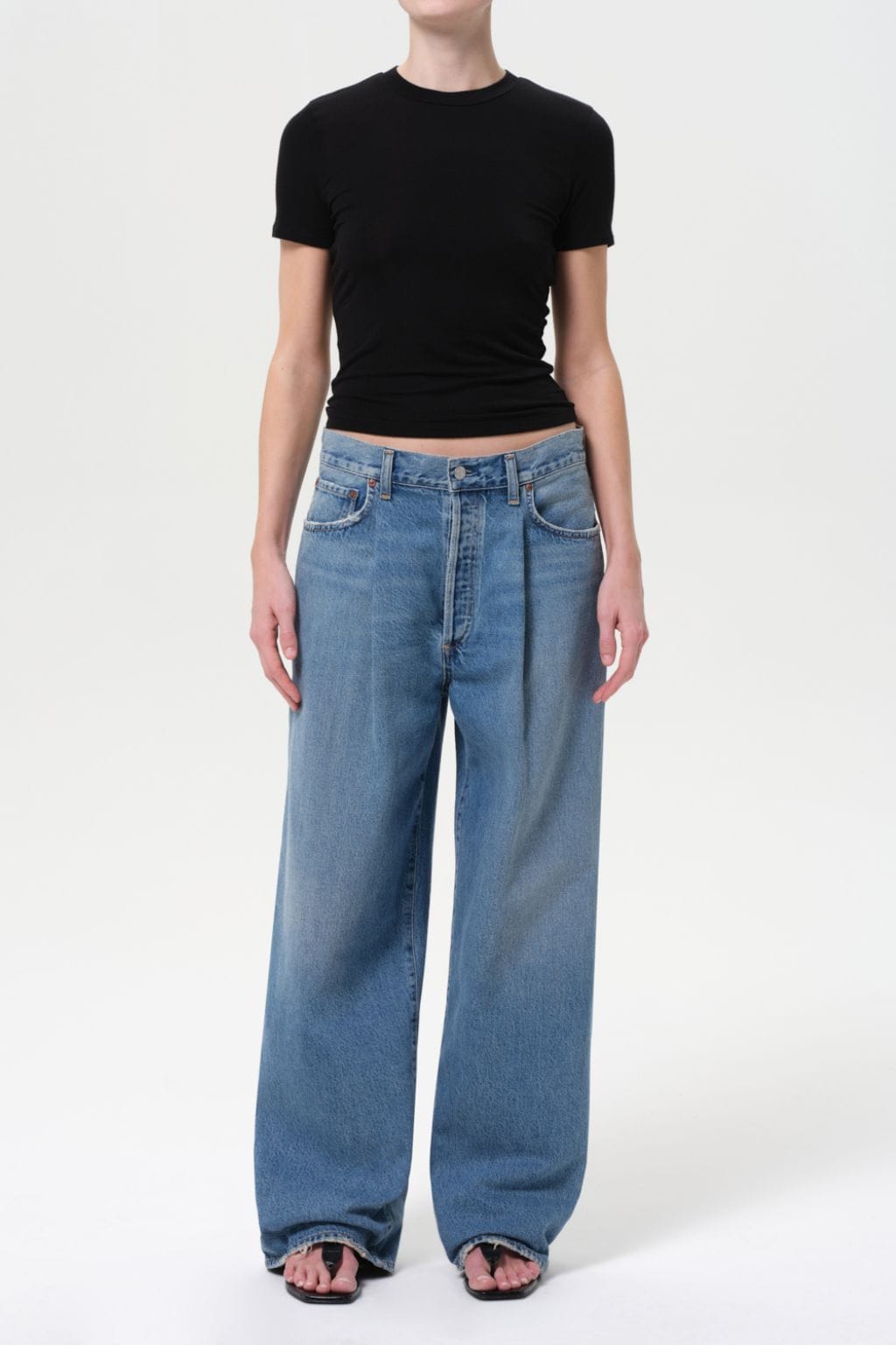 Person wearing black short-sleeve t-shirt and light blue pleated wide-leg denim jeans with a cropped waist.