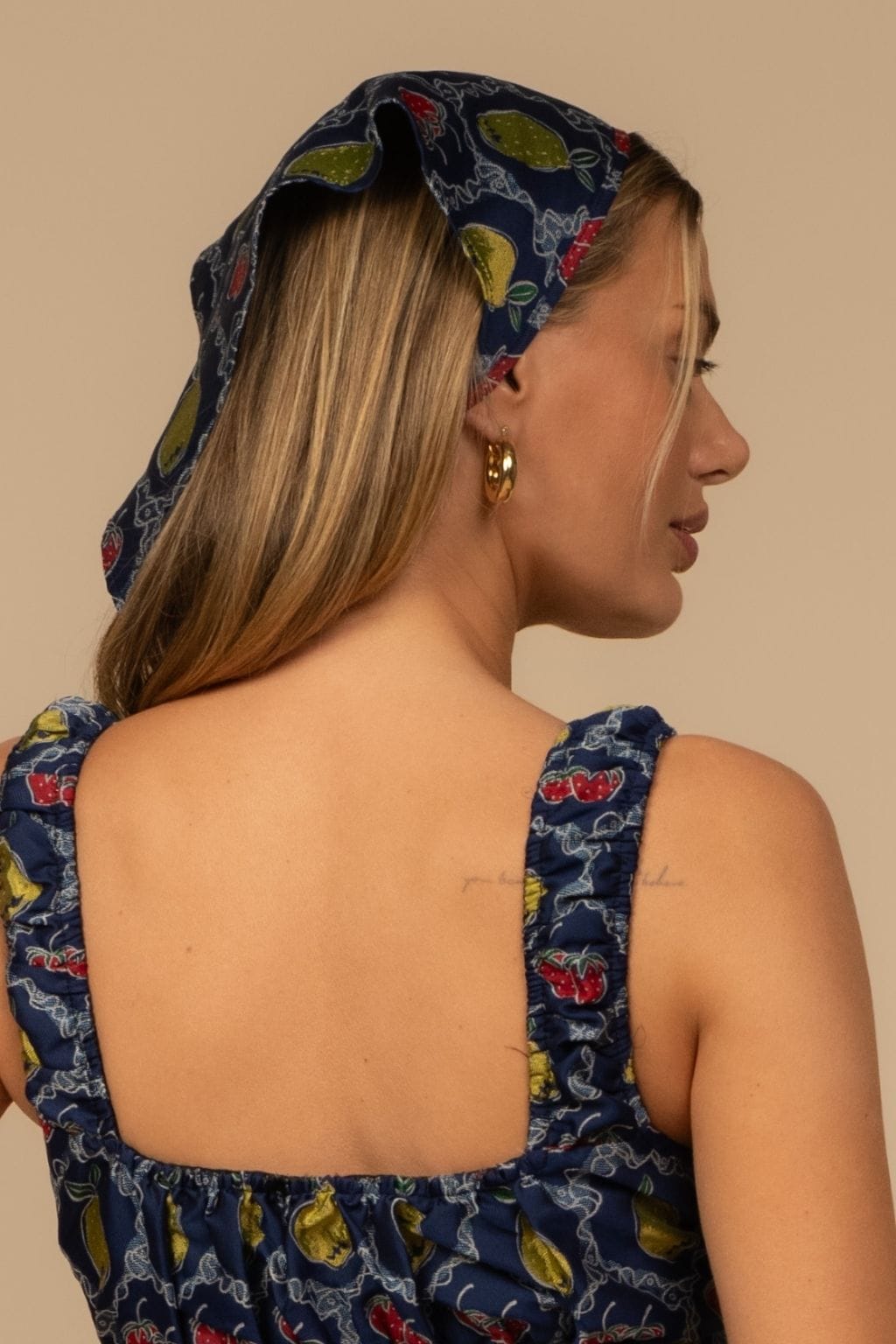 Navy scarf with yellow lemons and red berries jacquard pattern tied around hair as headwrap.