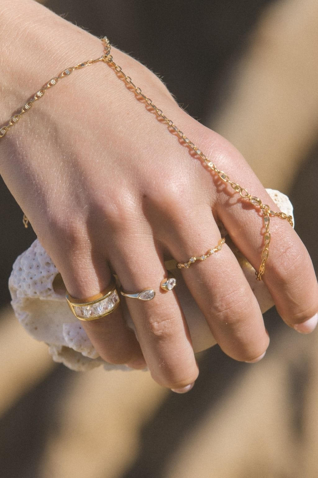 Gold hand chain with delicate links and crystal accents worn across the hand with matching ring.
