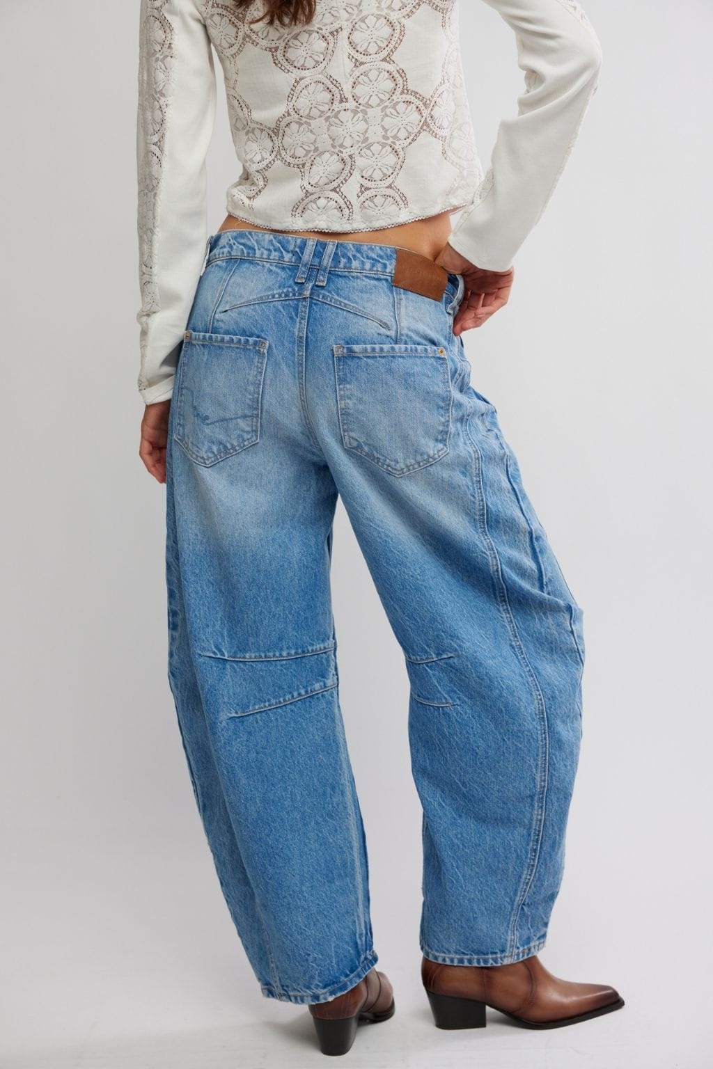 Light blue barrel jeans with wide leg, cropped length, and visible stitching details worn with a cream lace top.