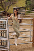 Woman wearing sleeveless maxi dress with geometric pattern in cream and olive tones, paired with white boots.