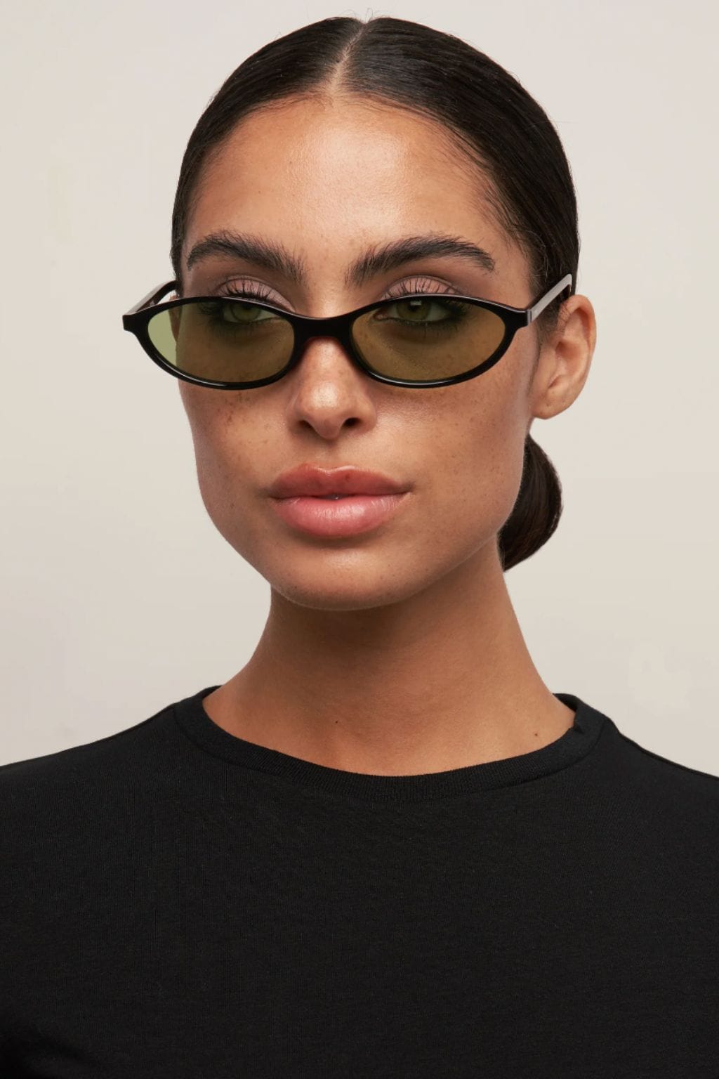 Black oval sunglasses with light green-tinted lenses worn by a person in a black shirt.