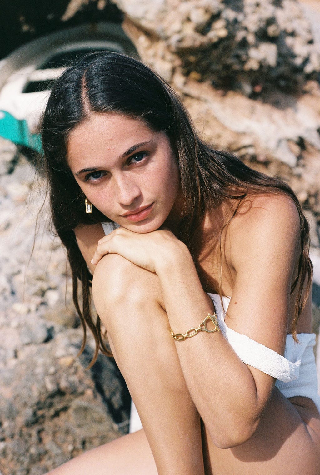 Gold chain bracelet worn on wrist against outdoor rocky background.