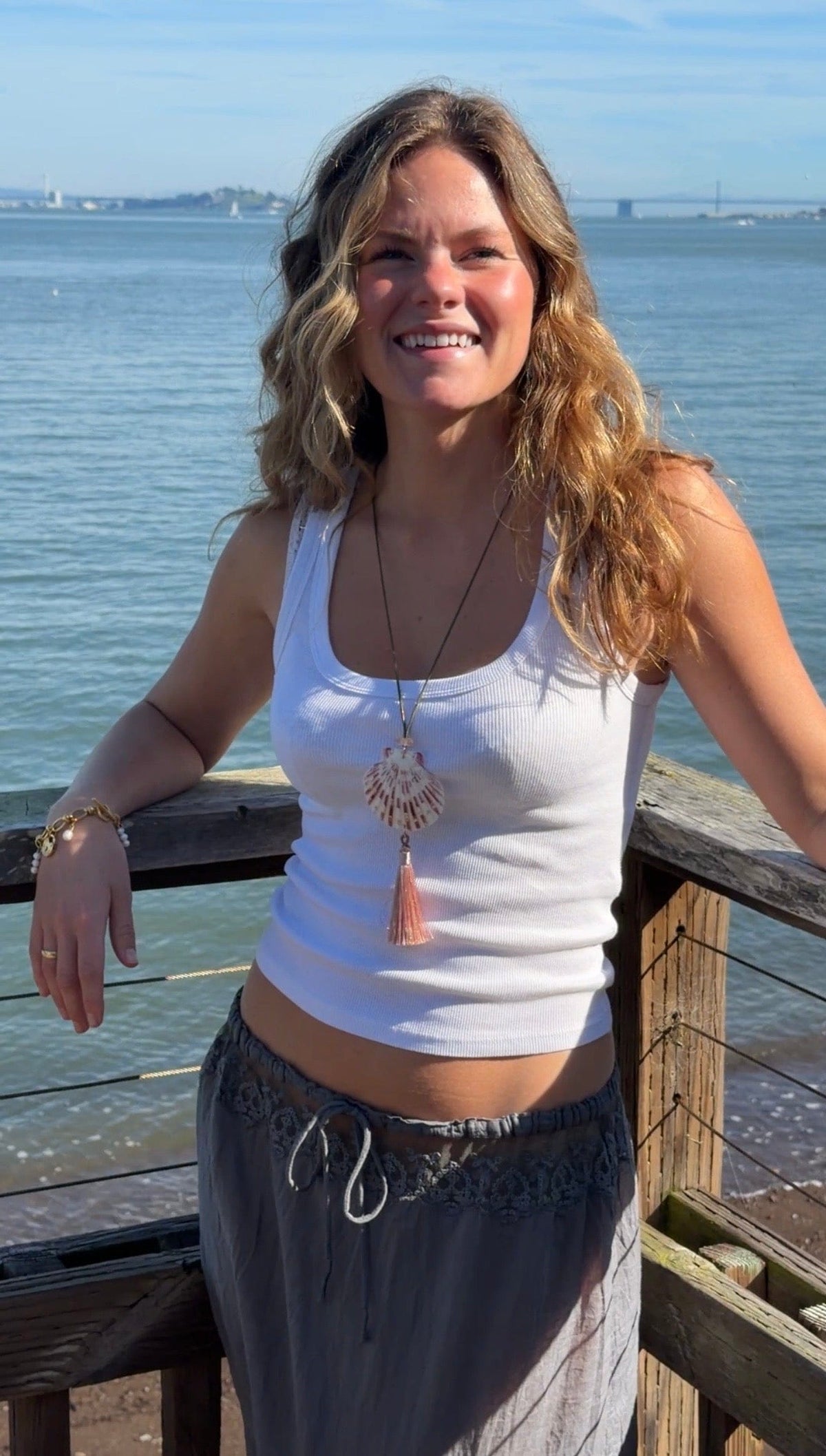 Shell-shaped pendant necklace with tassel charm worn on cord chain.