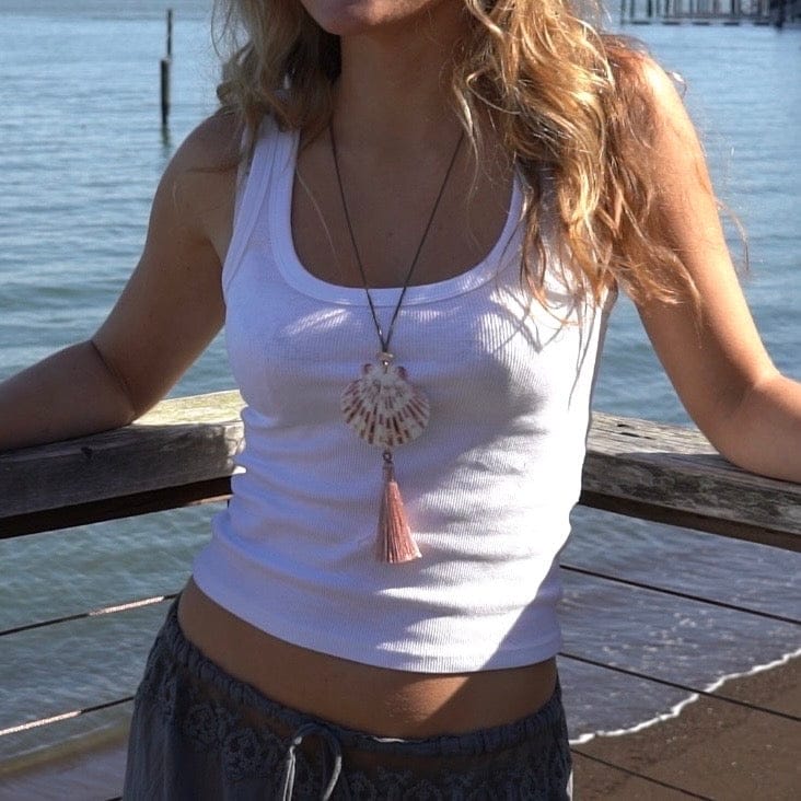 Long beaded necklace with fan-shaped pendant and coral tassel hanging from dark cord.