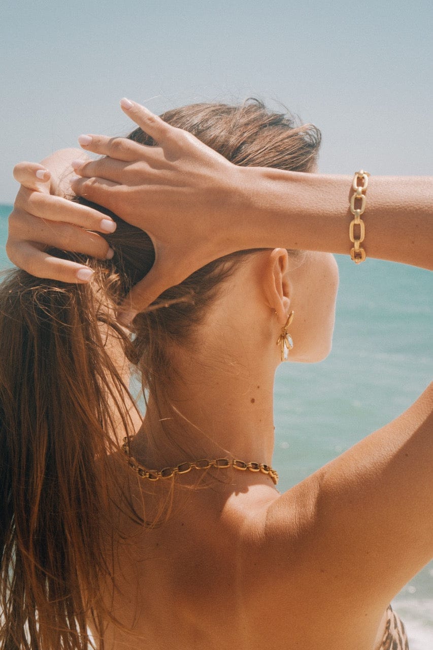 Gold chain link bracelet worn on wrist at beach setting.