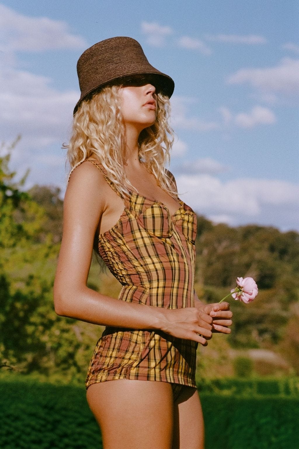 Brown woven bucket hat with black trim worn by person in plaid dress outdoors.
