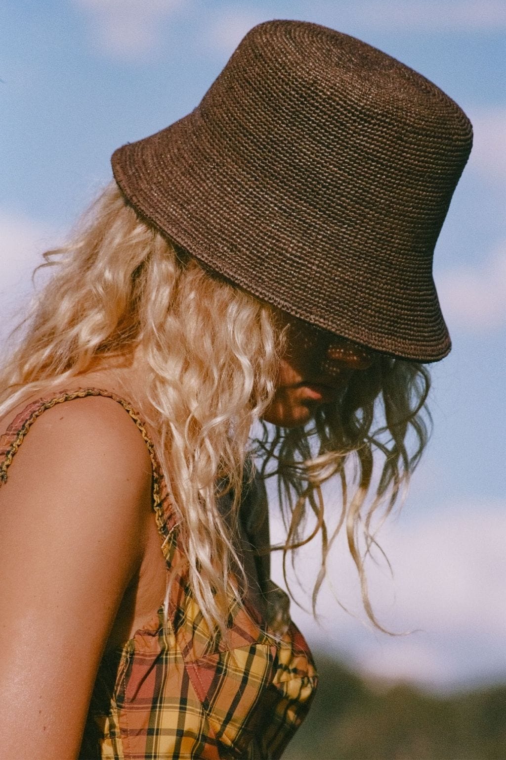 Brown woven bucket hat with textured fabric and sloped brim worn by person with long blonde hair.