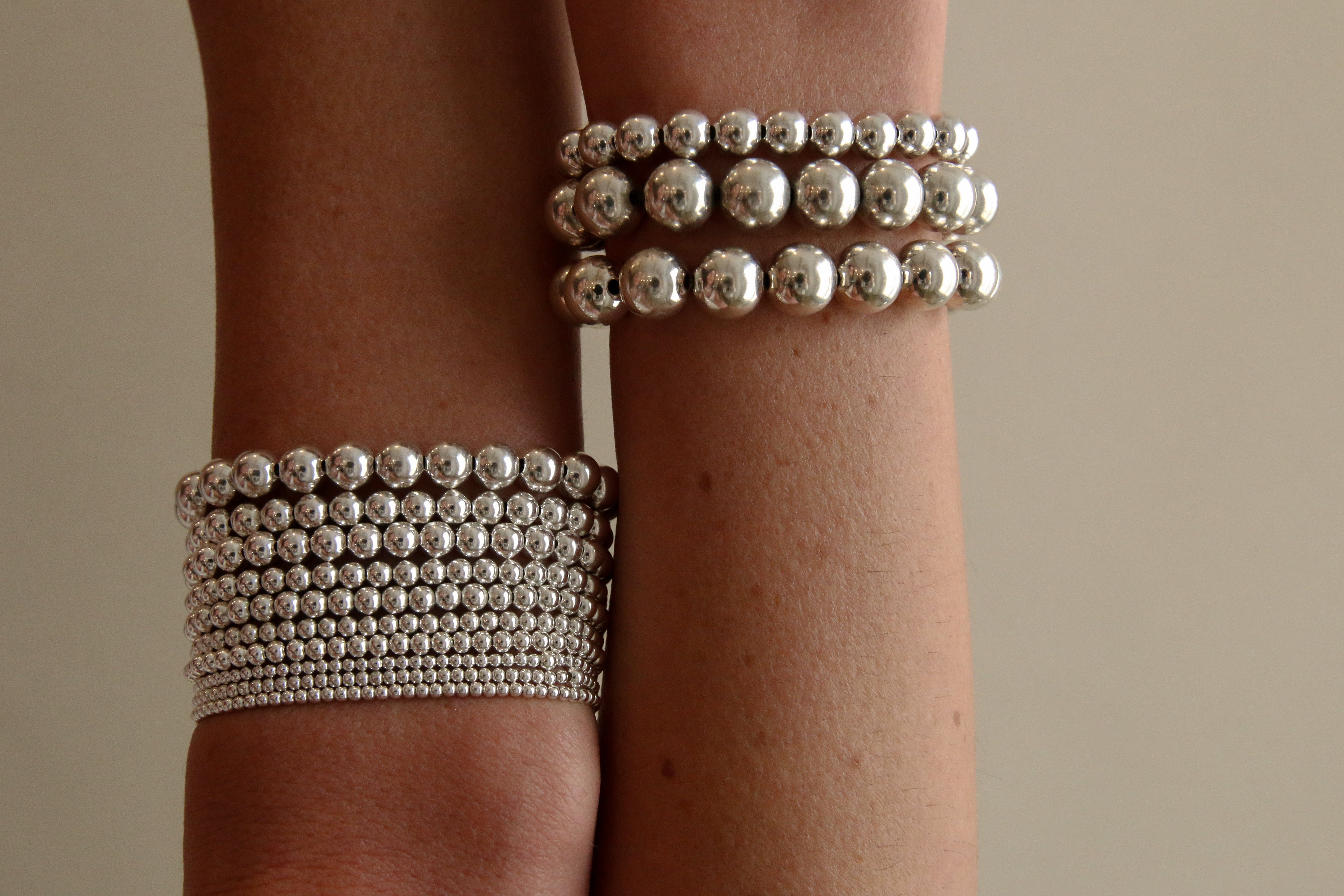 Silver-toned beaded bracelets worn on wrist, featuring 4mm spherical beads in three-strand and wide band styles.